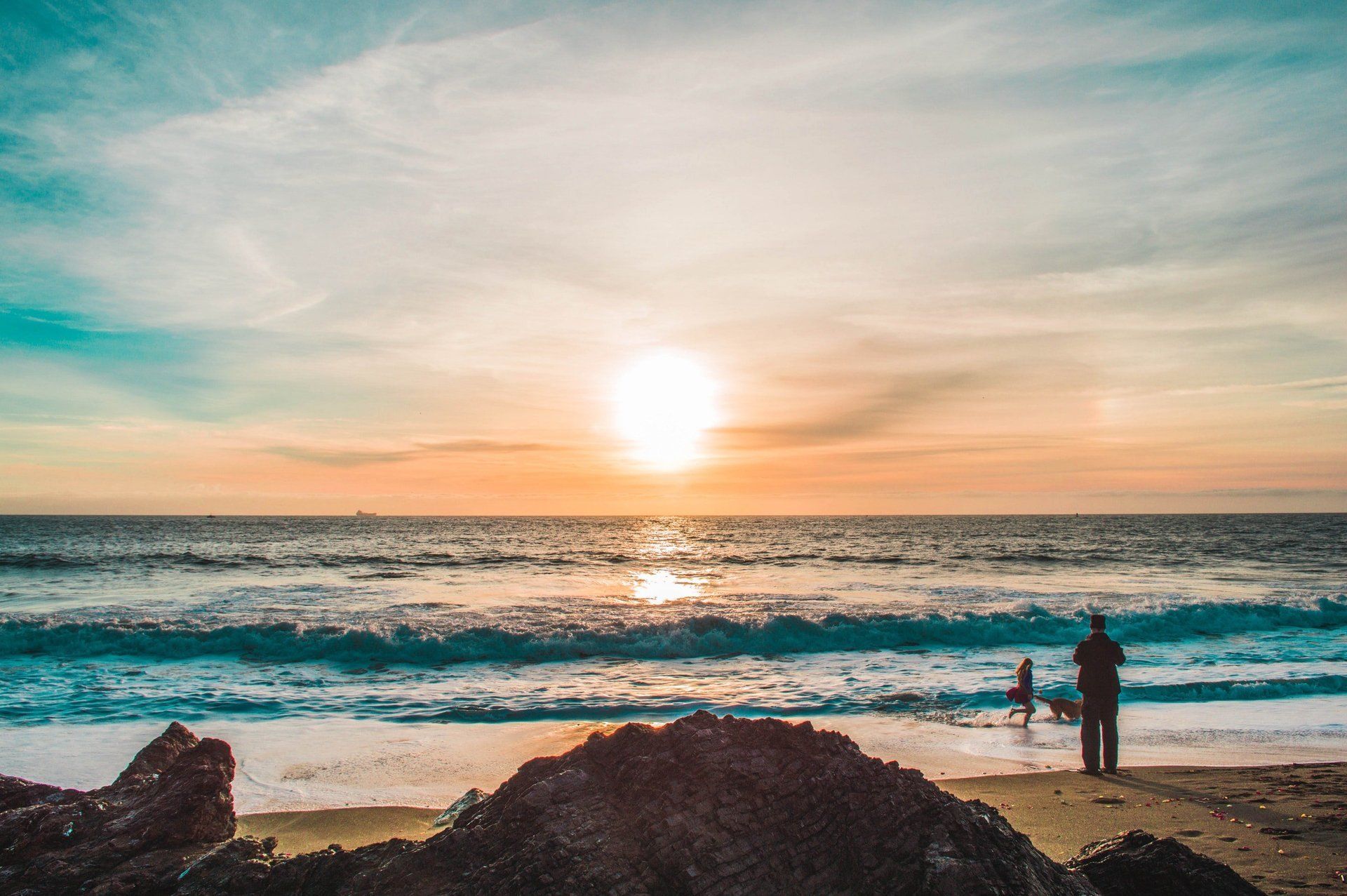 A man and a child are standing on a beach at sunset.