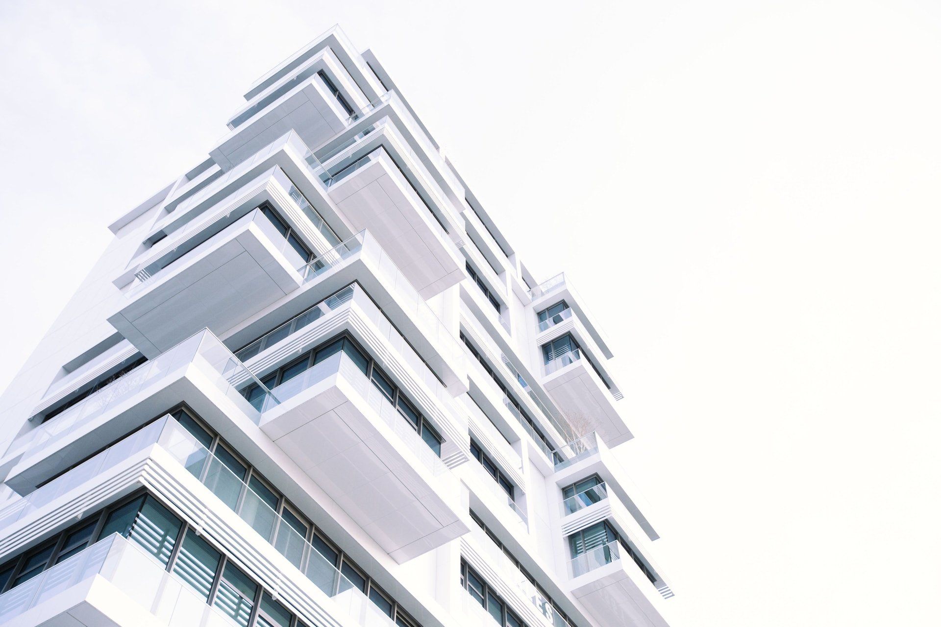 Mirando hacia un alto edificio blanco con balcones contra un cielo blanco.
