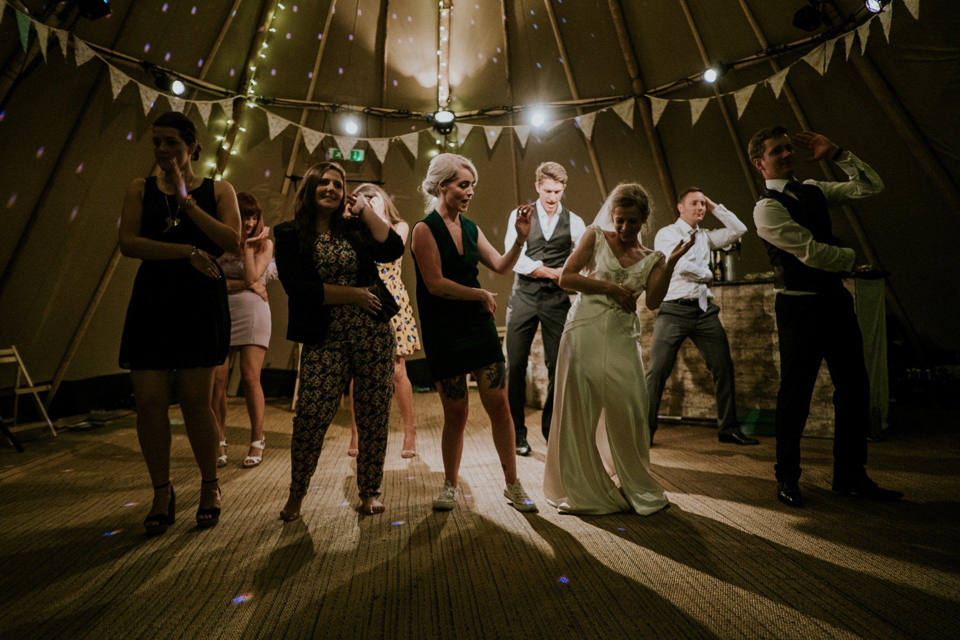 A group of people are dancing in a tent at a wedding reception.