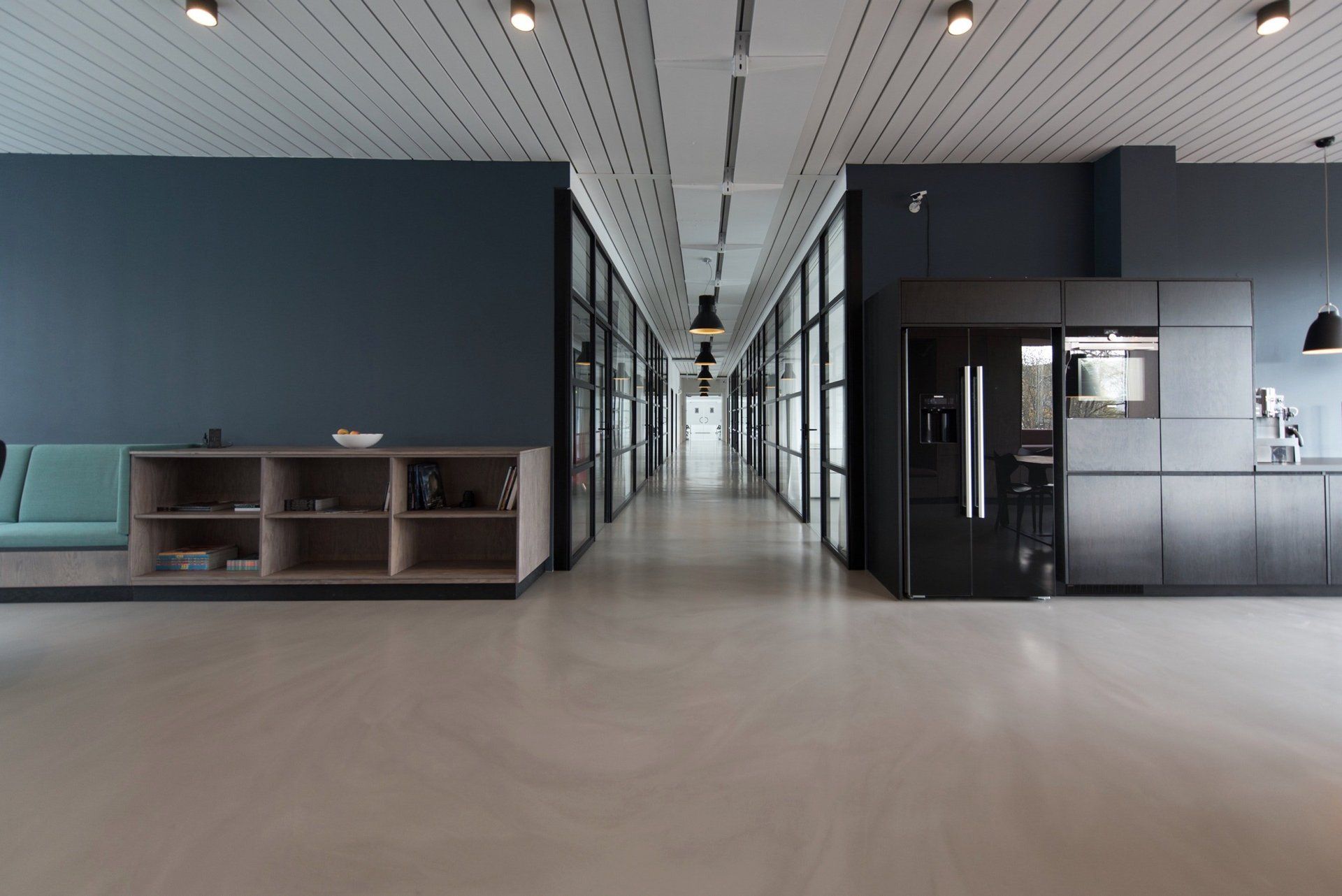View of a modern office interior corridor with glass boardrooms on either side of the corridor and an open atrium painted in dark blue by painters and decorators London