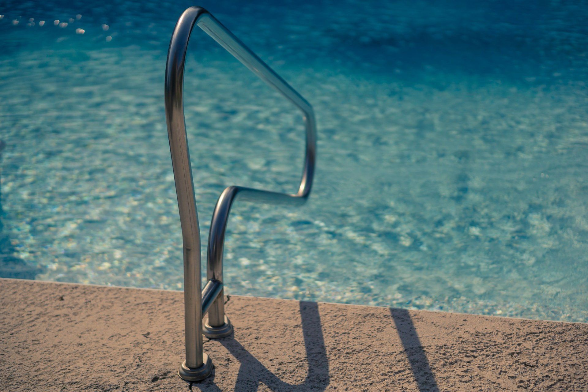 A close up of a metal railing leading to a swimming pool.