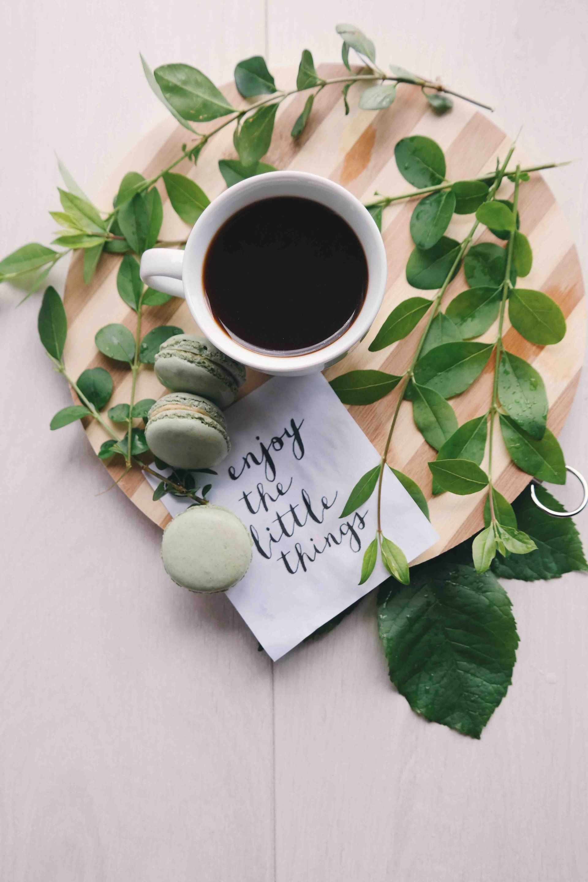 A cup of coffee is on a wooden tray with leaves and macarons.
