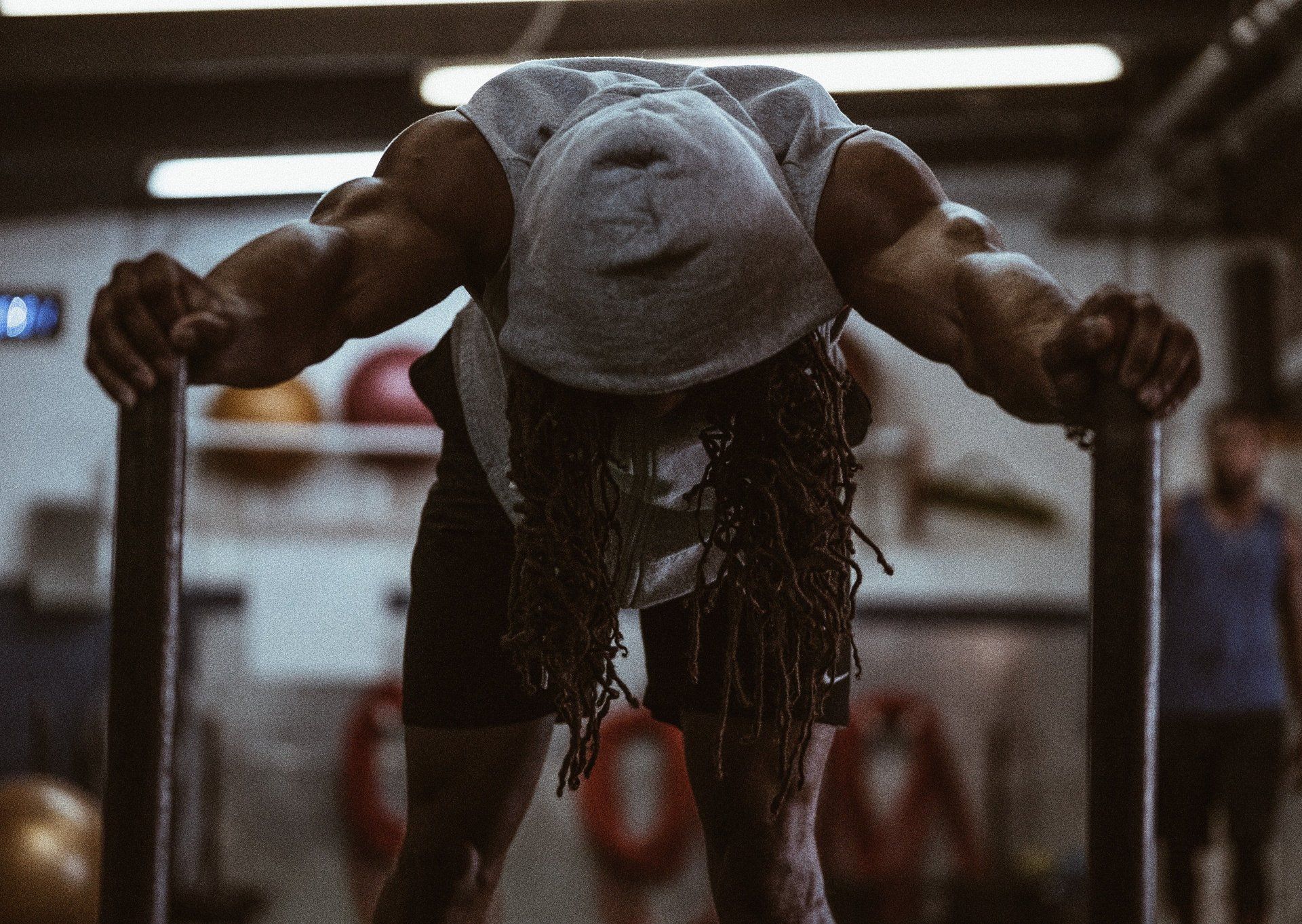 Person doing a push-up in a gym, wearing a white cap and dark clothing, seen from the front.