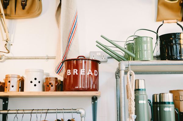 A red bread bin is sitting on top of a wooden shelf.