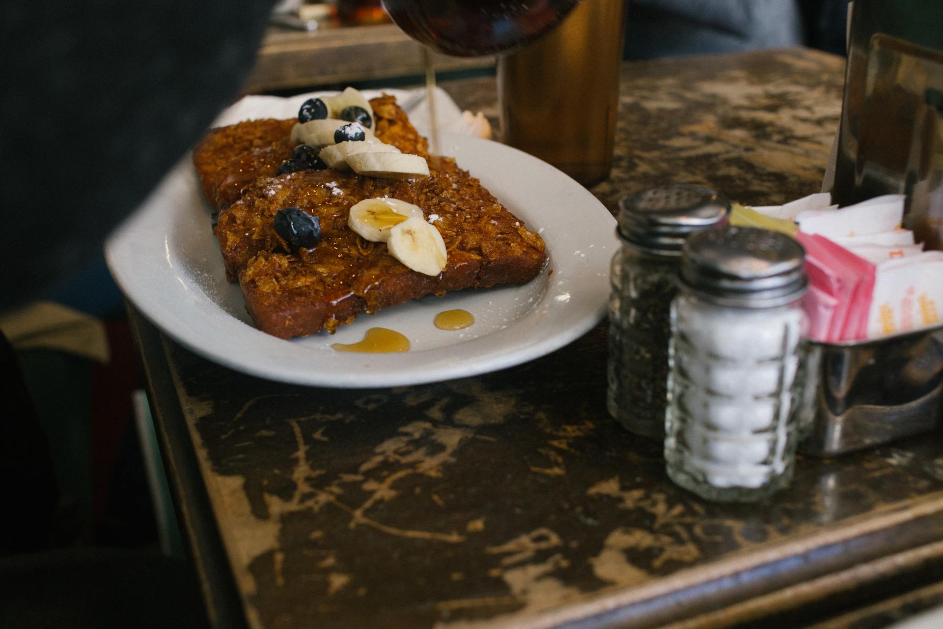 A plate of french toast with bananas and blueberries on a table.