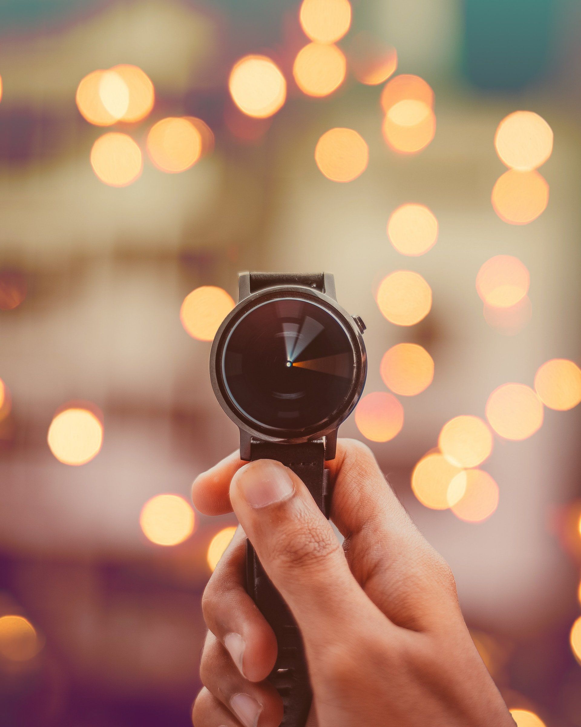 Hand holding a black smartwatch, with blurred bokeh lights in the background.