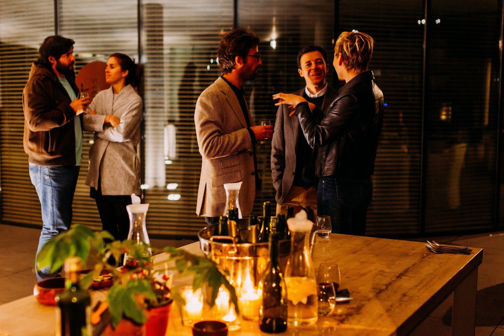 A group of people standing around a table with wine bottles and candles