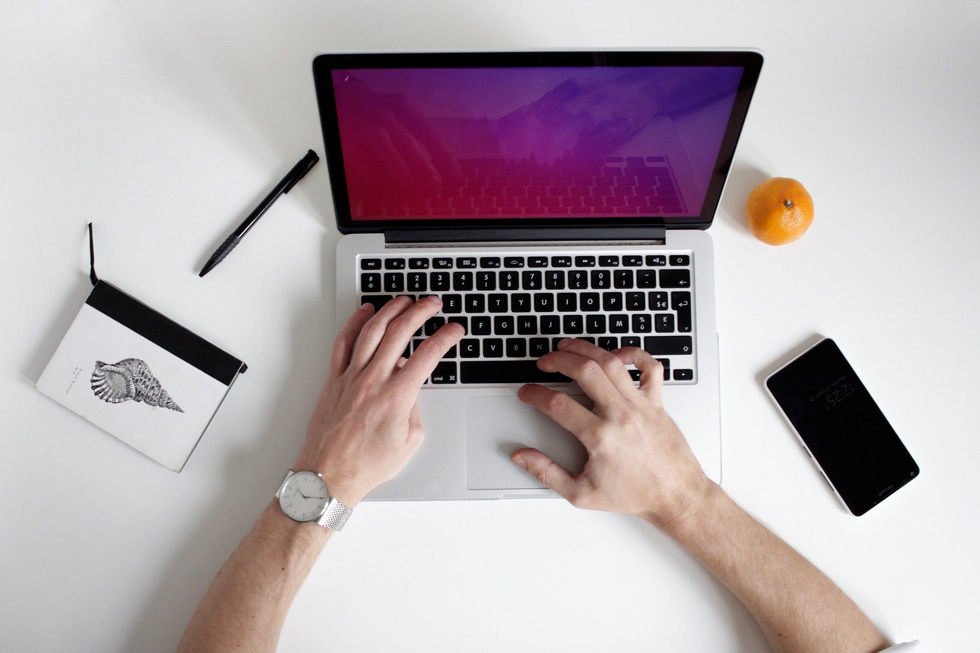 A person is typing on a laptop computer while wearing a watch.