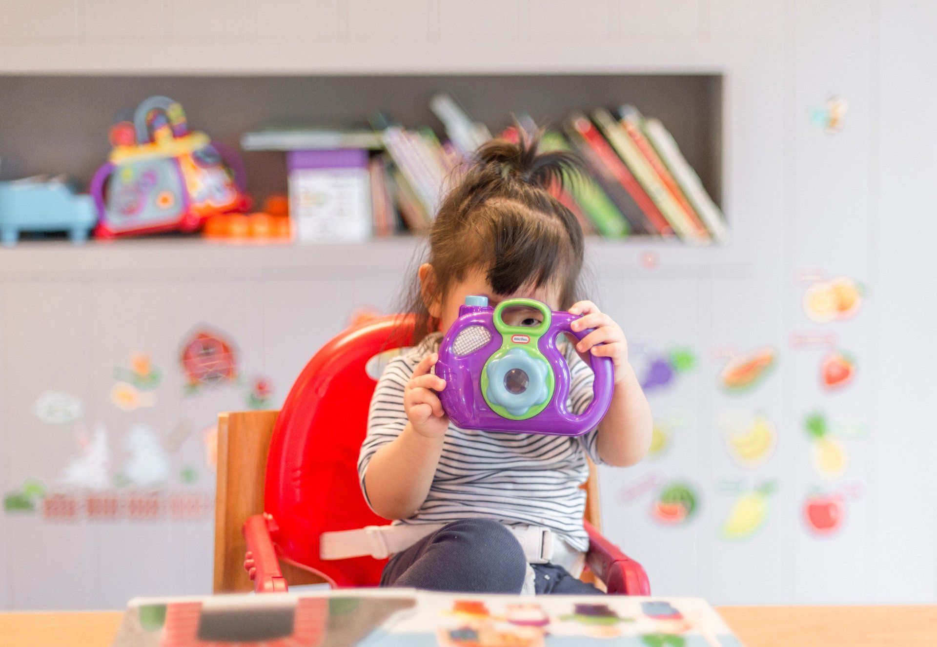 A little girl is sitting in a high chair holding a toy camera. Dramatherapy Ireland
