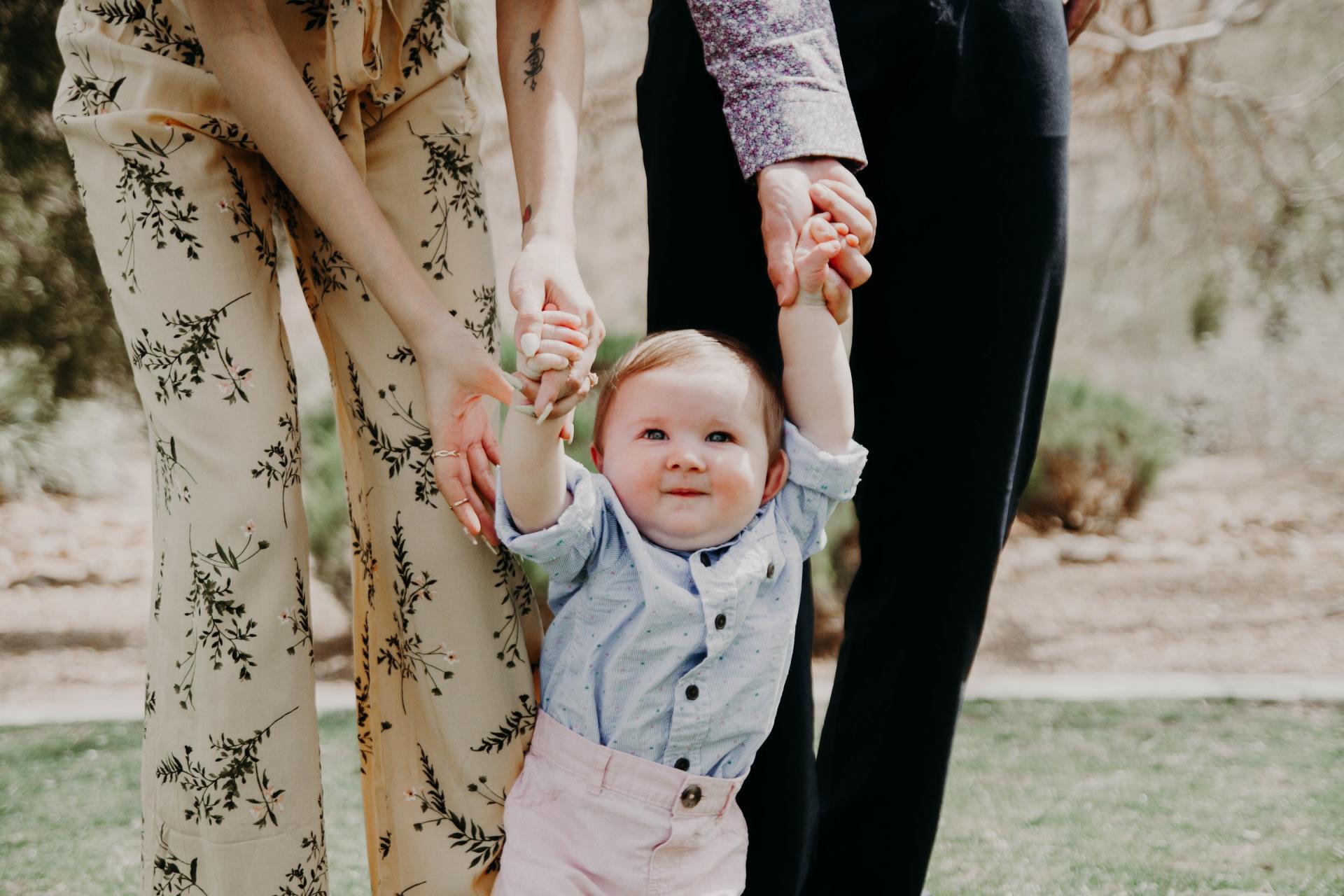 Child held up by two adults, smiling. Outdoors, grassy area.