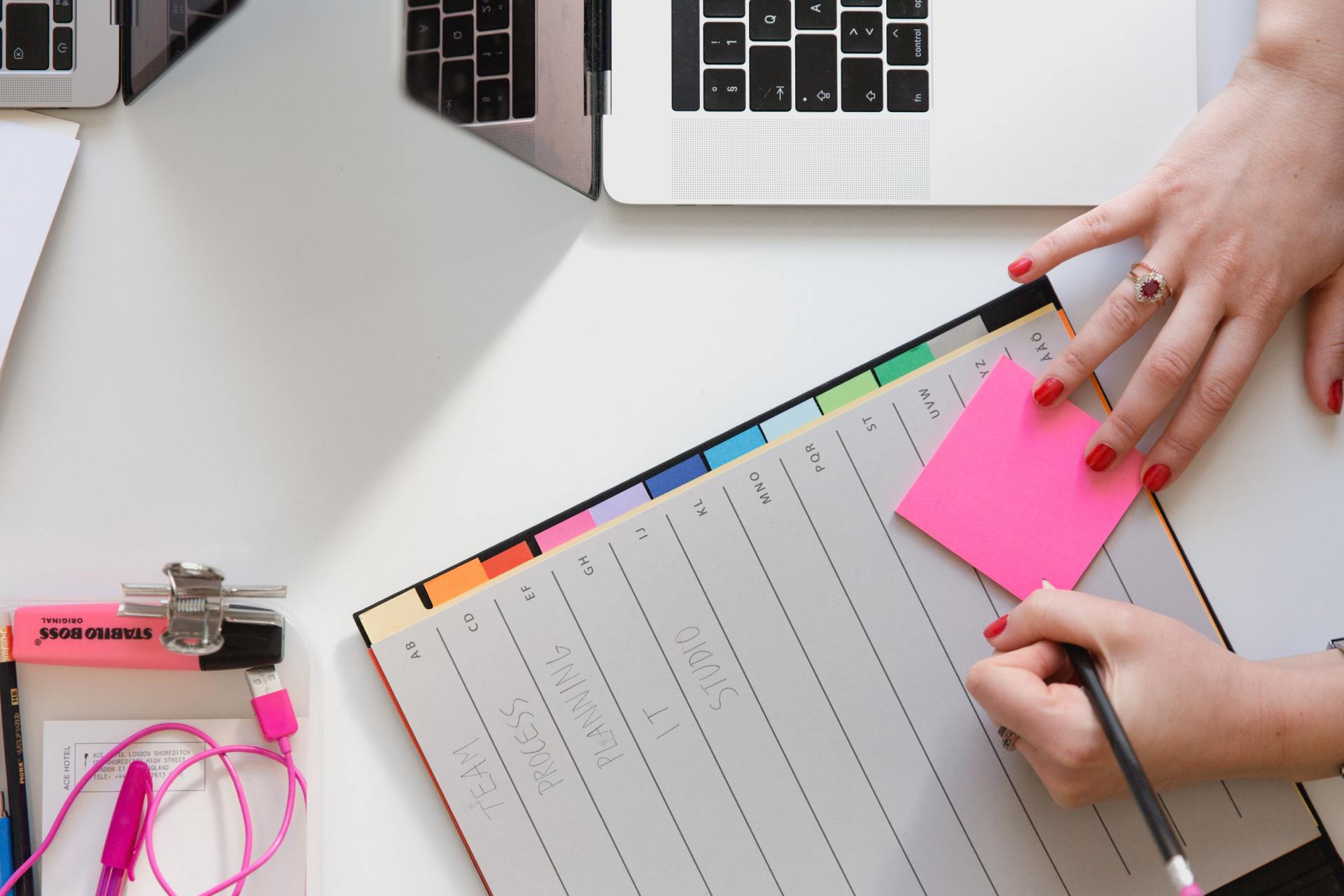 A person is holding a pink sticky note on top of a notebook.