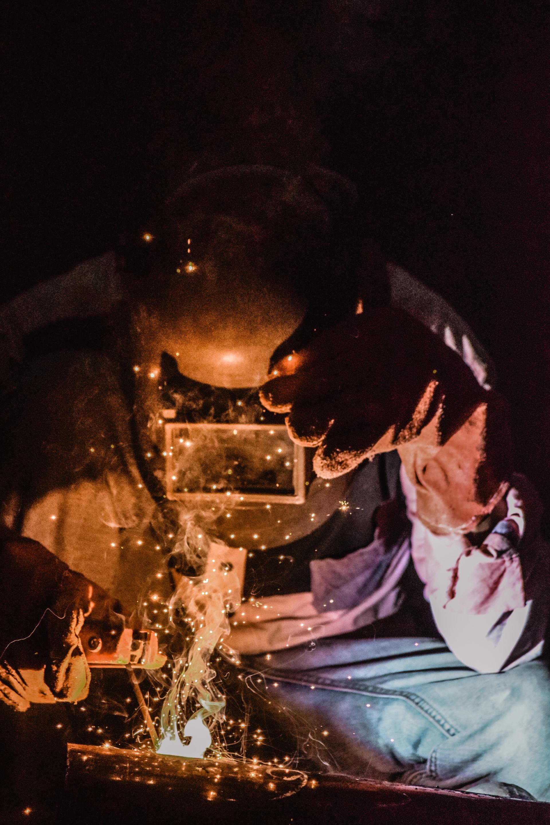 Welder in protective mask sparks flying in a dark workshop