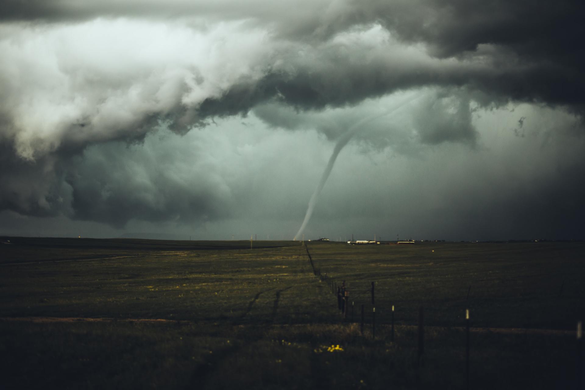 A tornado is coming through the clouds over a field.