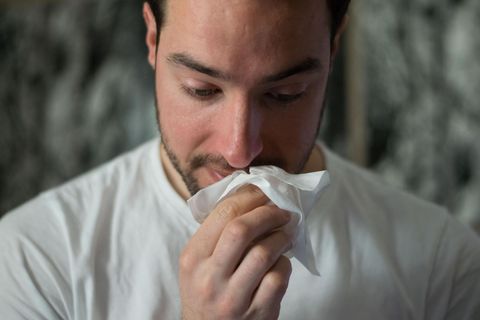 Man in white shirt blowing nose with a tissue.