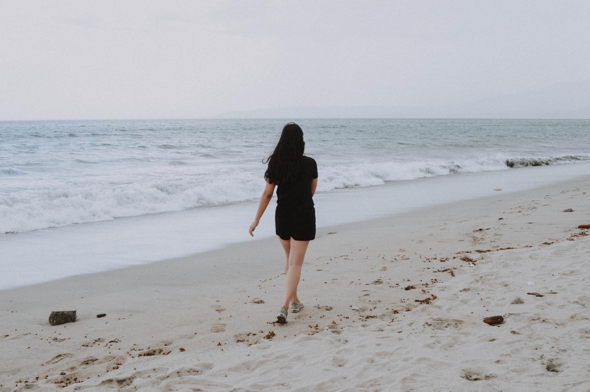 A woman in a black dress is walking on the beach.
