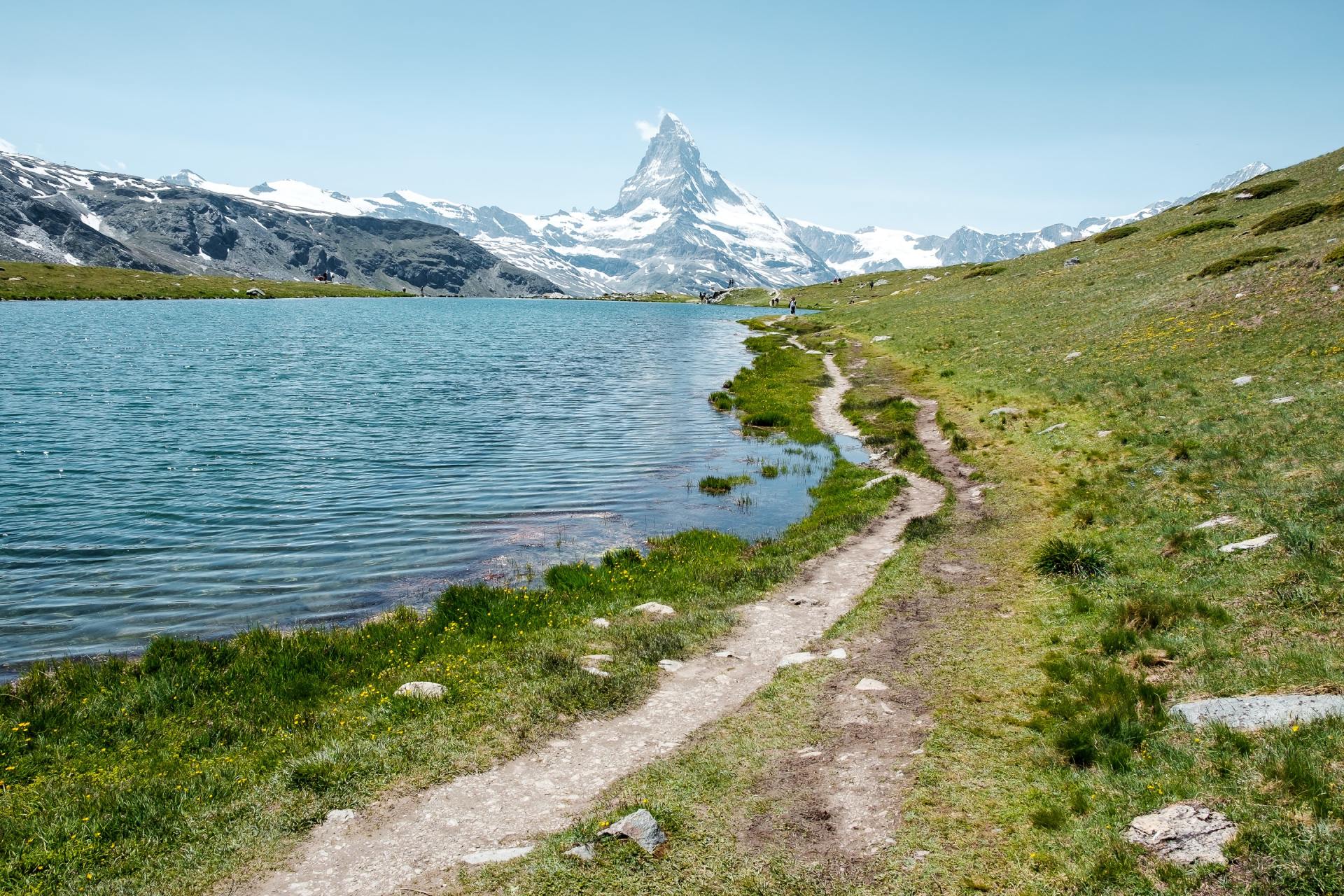A dirt path leading to a lake with a mountain in the background.