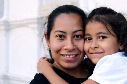 compre el medicamento a precio muy bajo Dos personas sonrientes se abrazan en el interior, cerca de una ventana luminosa.