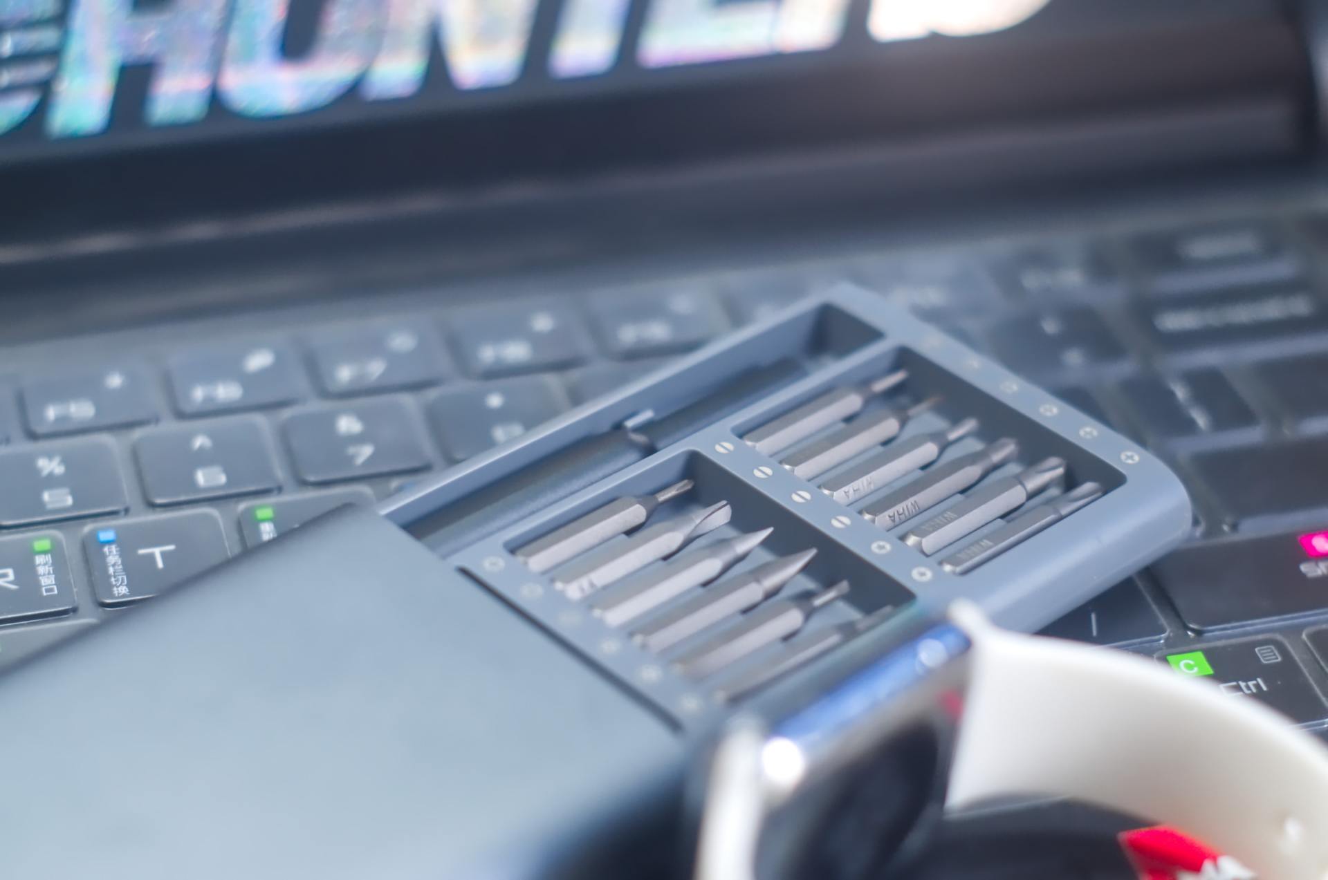 Open tool kit with bits on a laptop keyboard beside a white mug