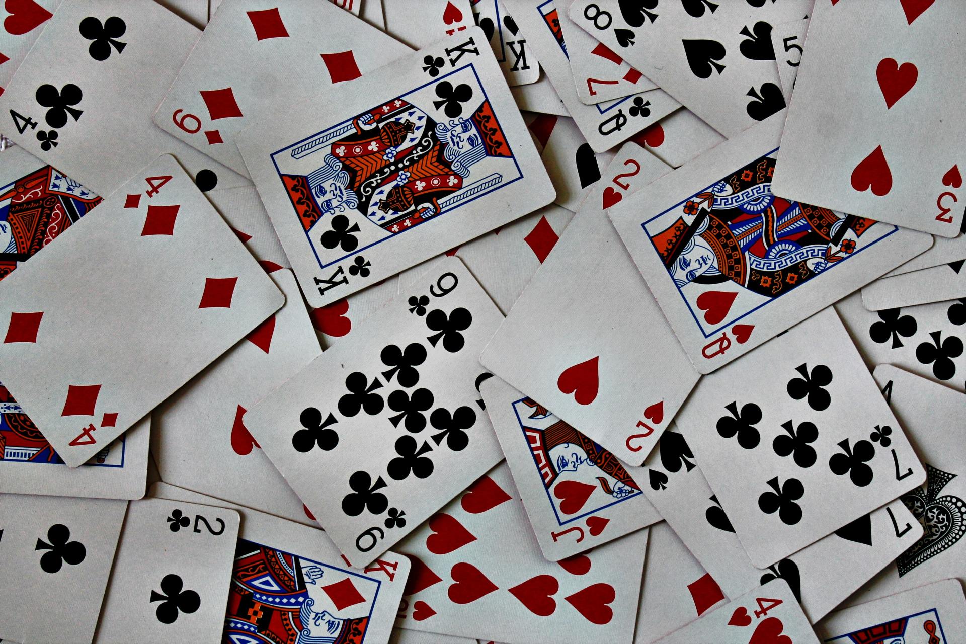 Scattered playing cards, mostly hearts and clubs, with a few face cards on a white background