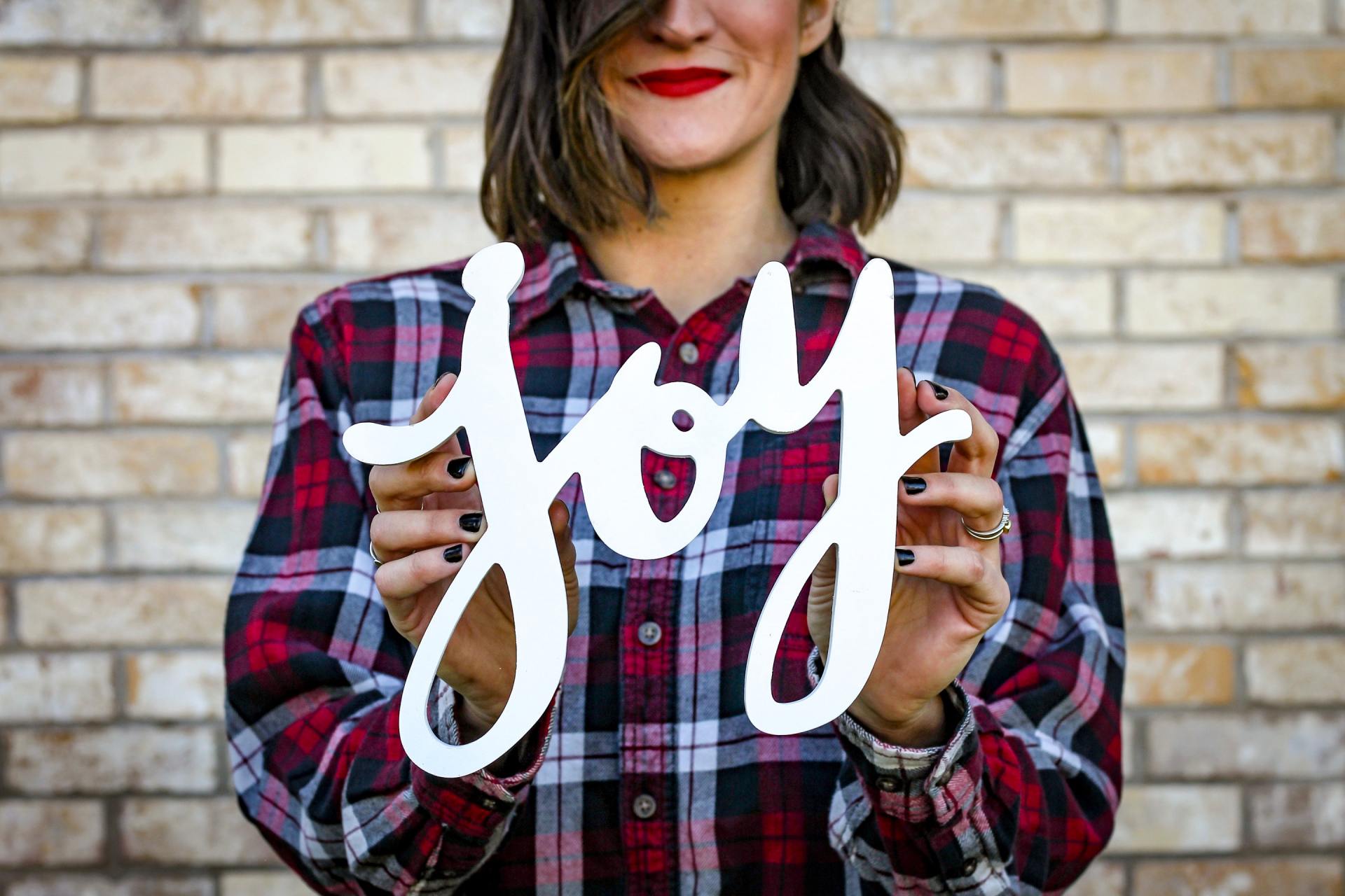 A woman in a plaid shirt is holding a sign that says joy.