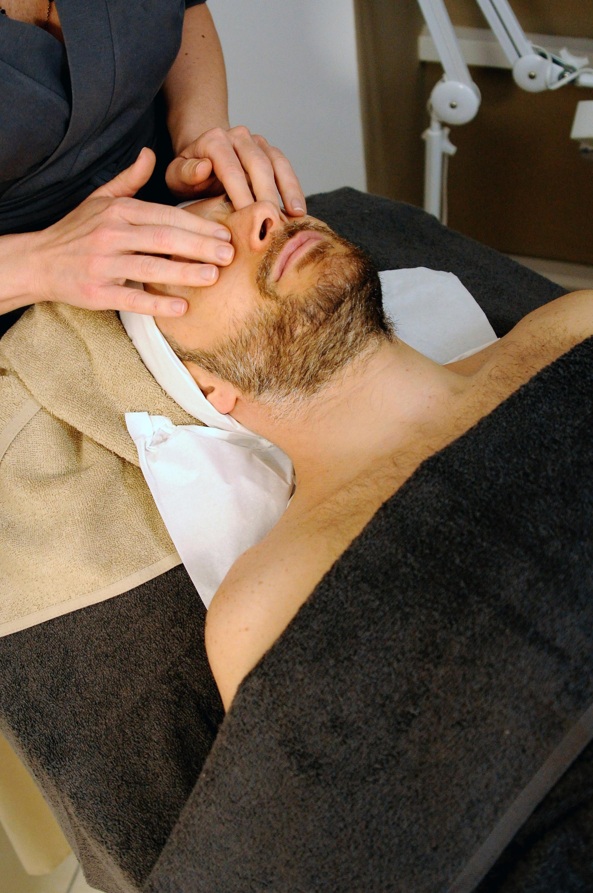 Facial massage treatment with hands on a man’s face and towel draped over his chest