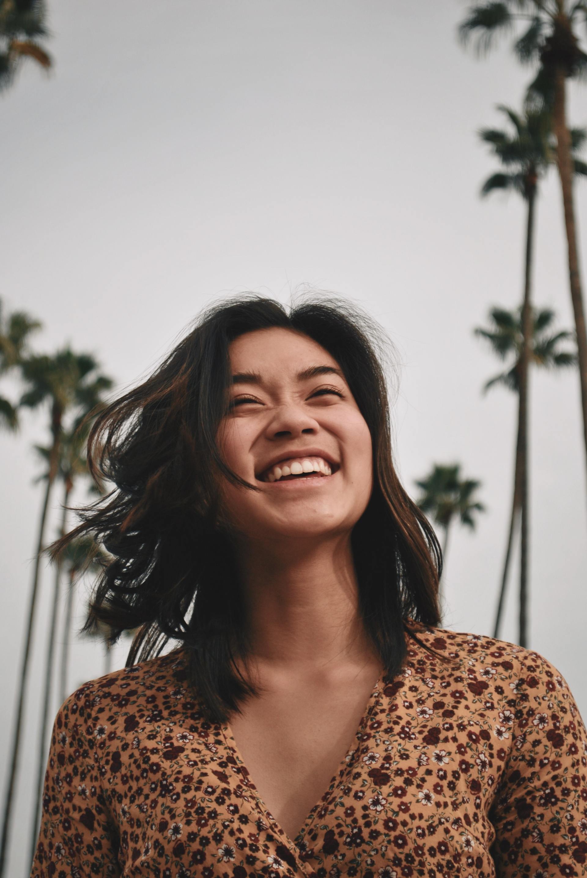 A woman in a leopard print shirt is smiling in front of palm trees.