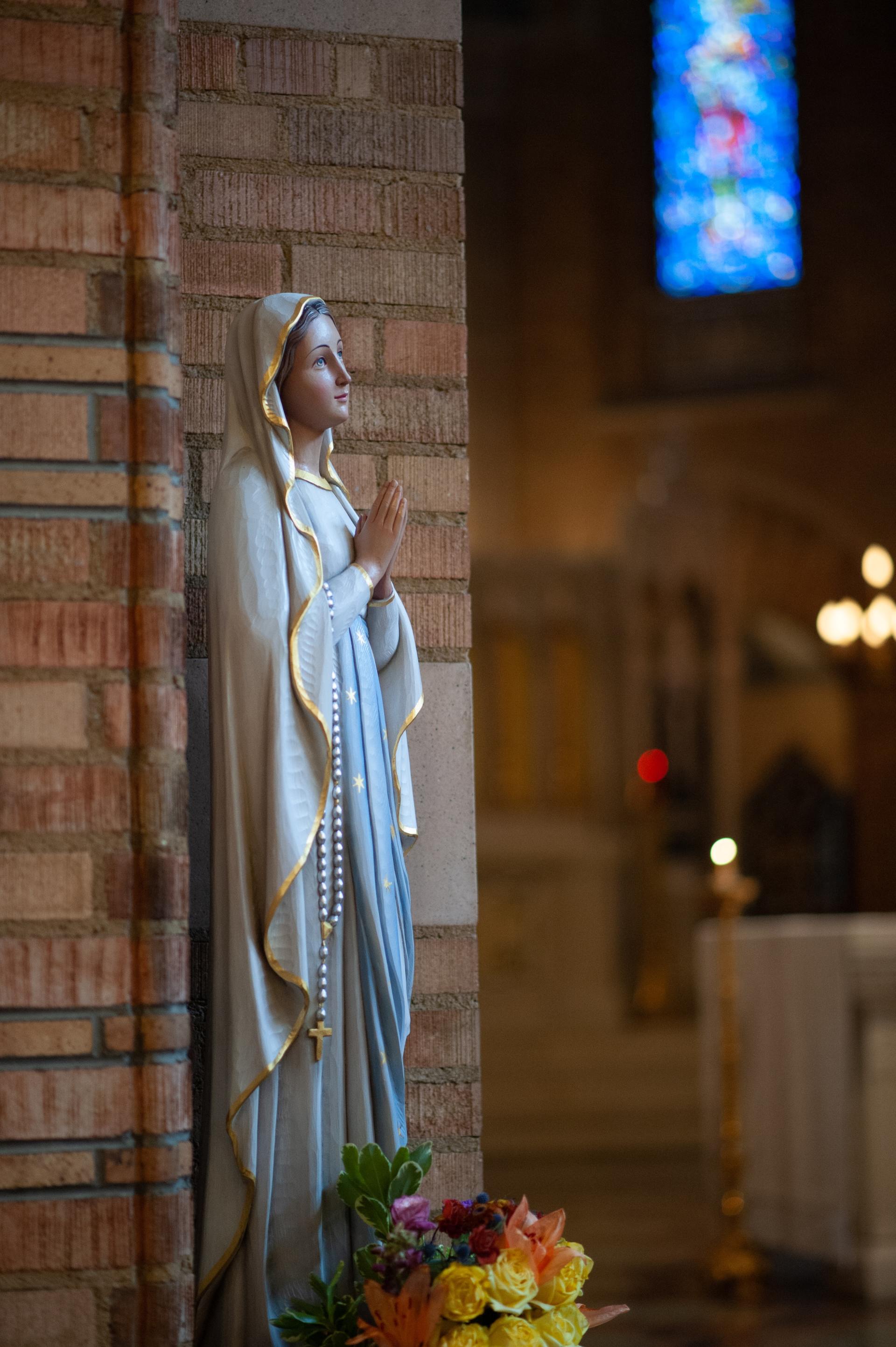 A statue of the virgin mary in a church with a stained glass window in the background.
