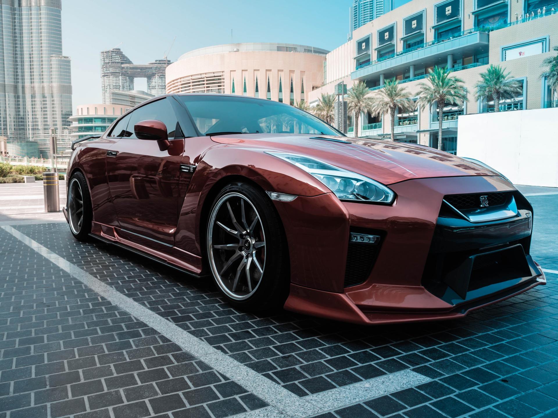 Maroon sports car parked on a city street with modern buildings in the background