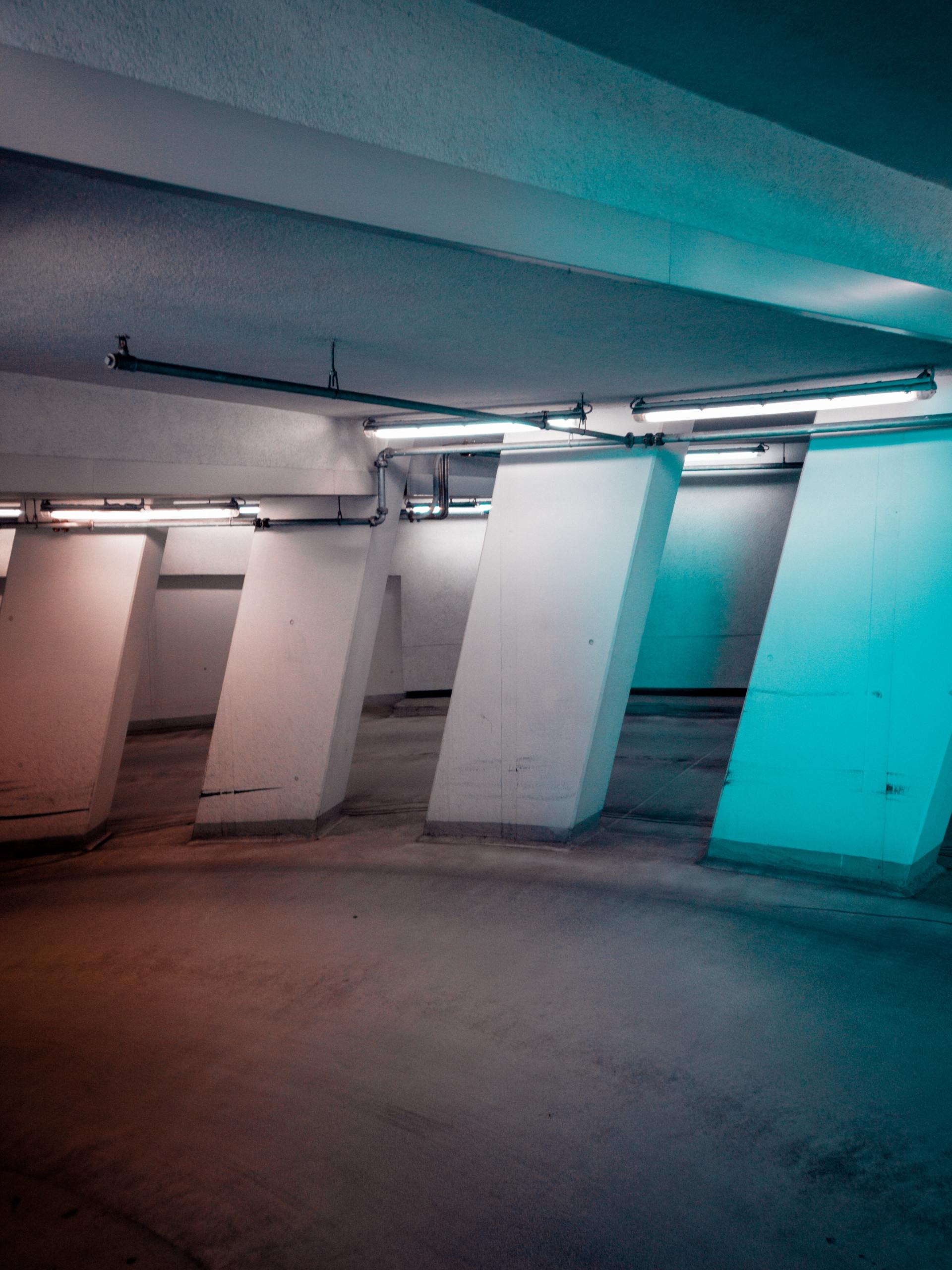Concrete columns in a stark, dimly lit parking garage with blue and orange lighting.