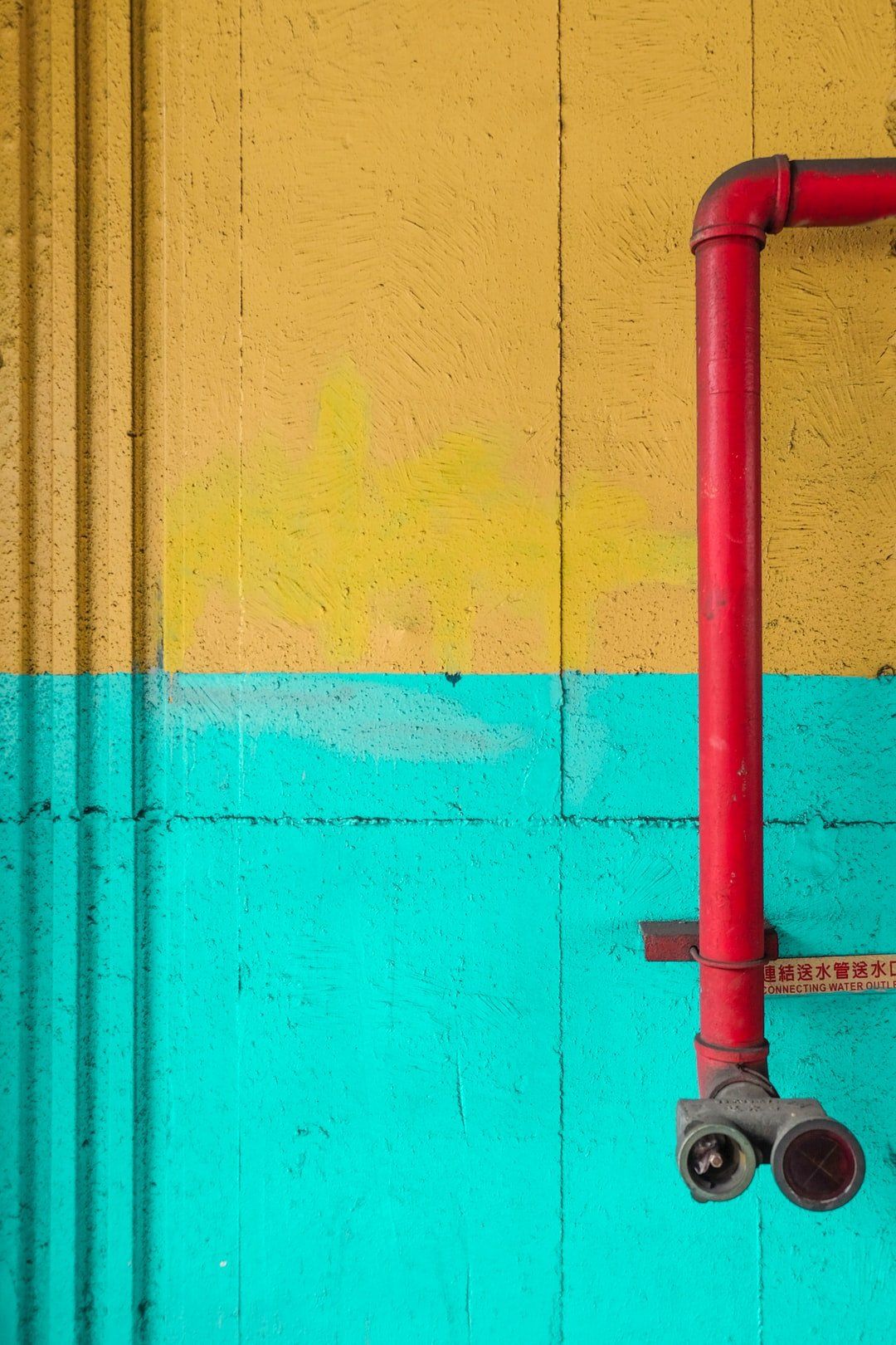 Red pipe on a yellow and teal textured wall.