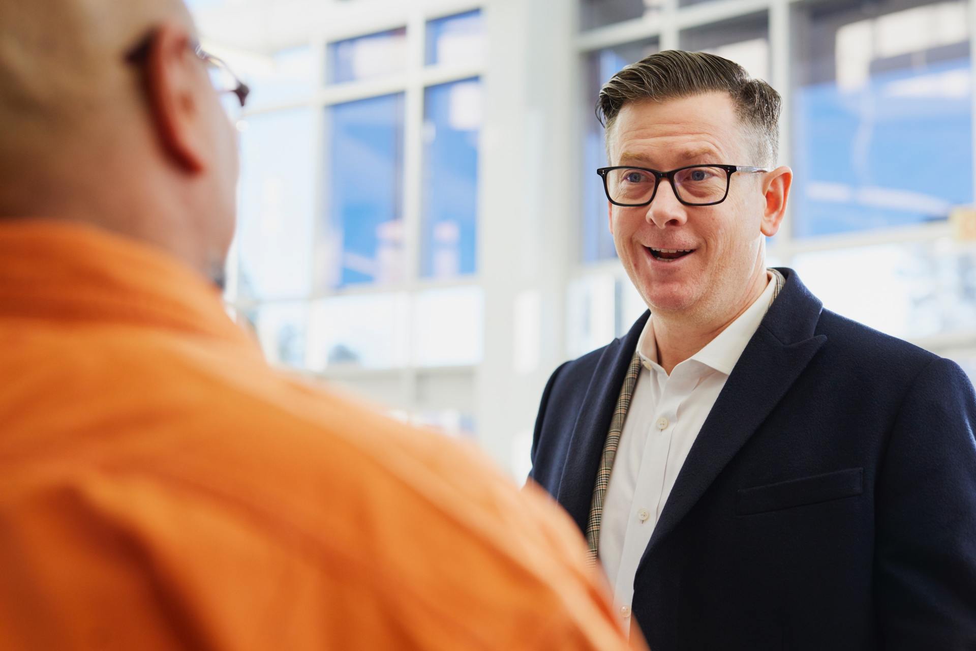 Two people talking in a bright office, one in an orange shirt and one in a dark blazer, smiling