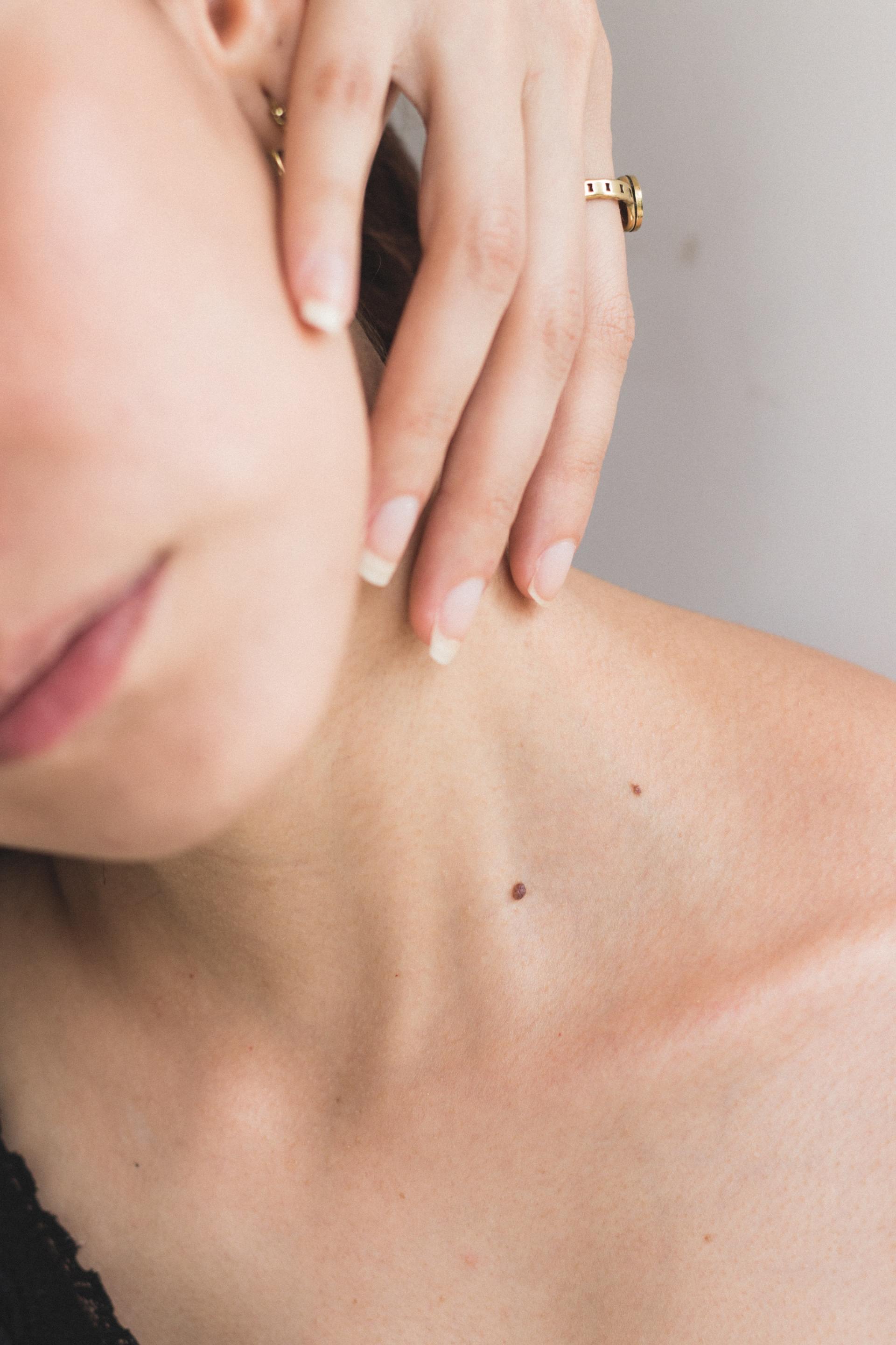 A close up of a woman 's neck and face with a ring on her finger.