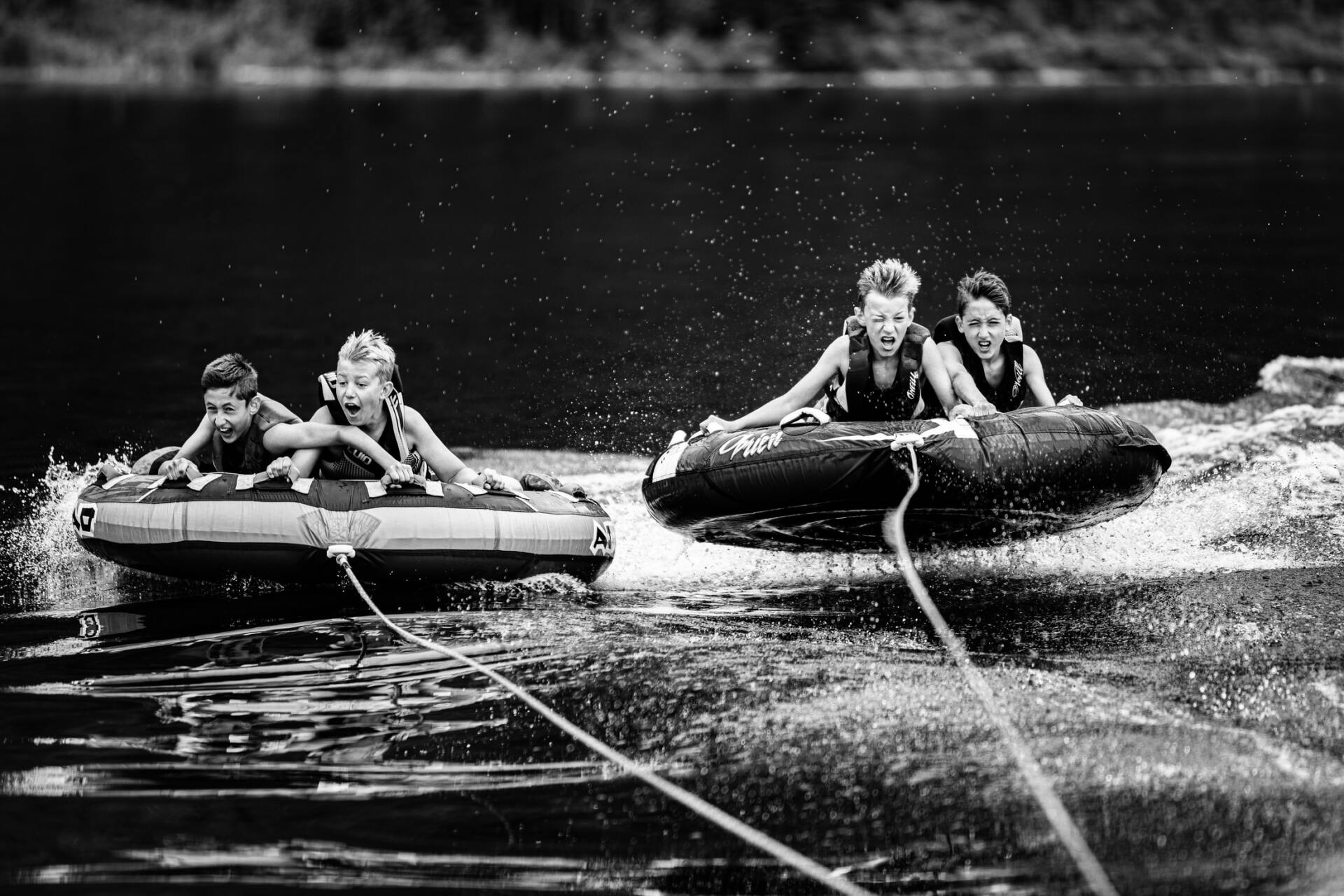 4 children on 2 inner tubes being pulled by boat