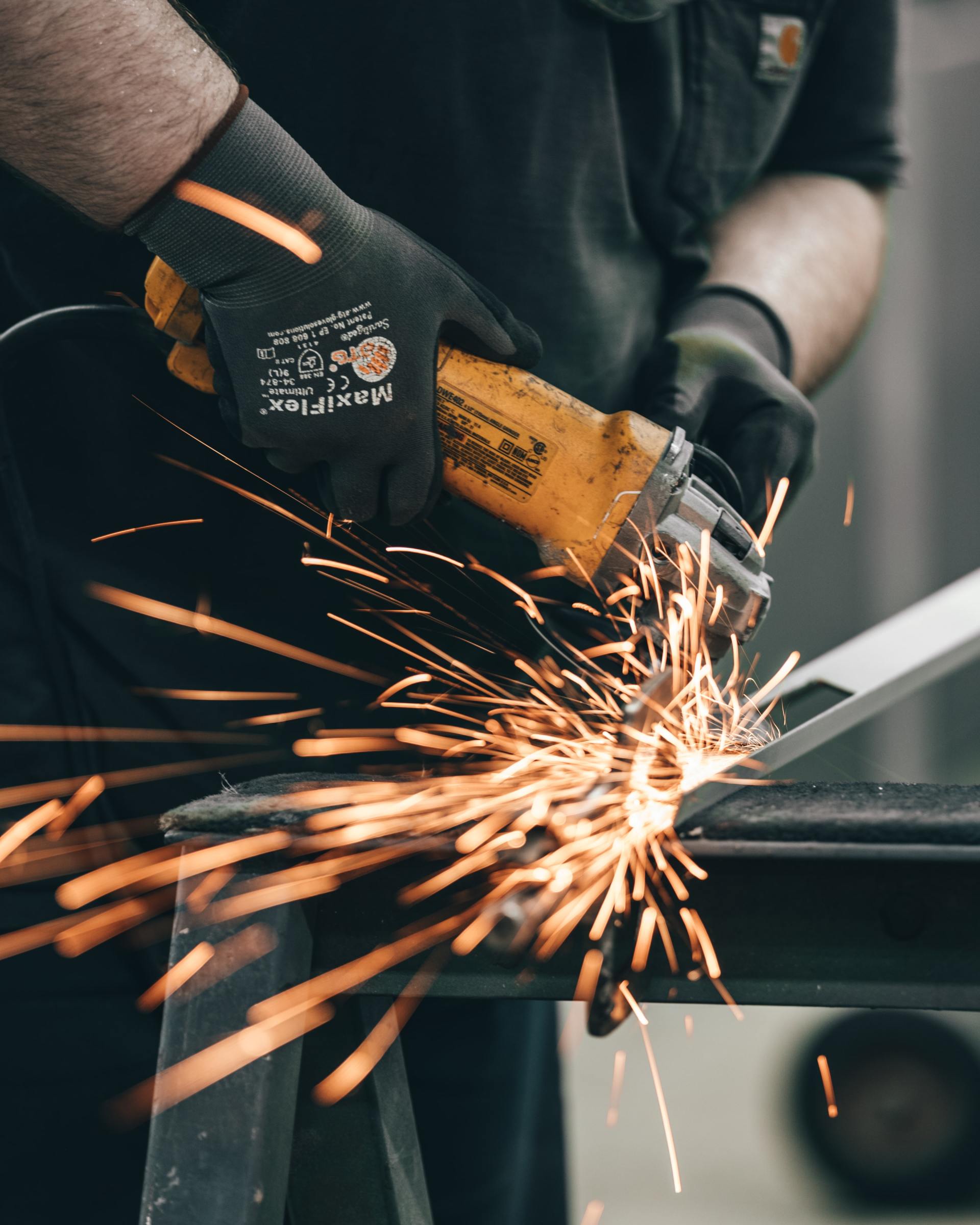 Worker using a yellow angle grinder, sparks flying as metal is cut in a workshop