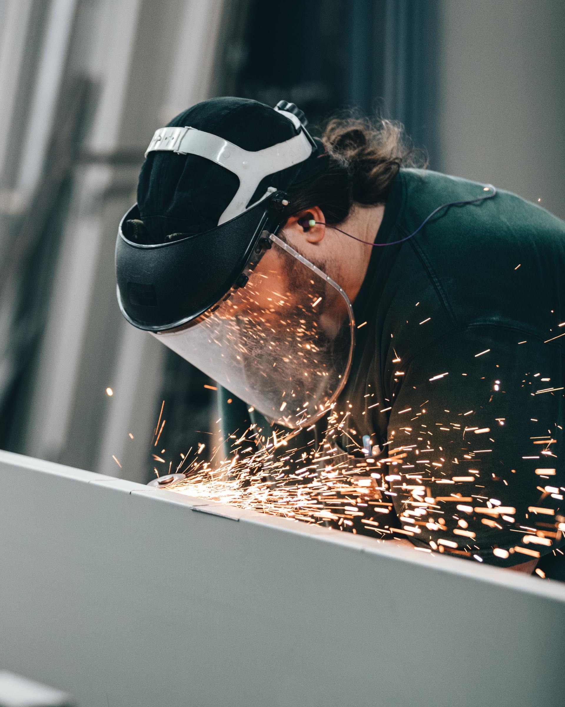 Worker using a face shield sparks metal with a grinder, scattering bright orange sparks