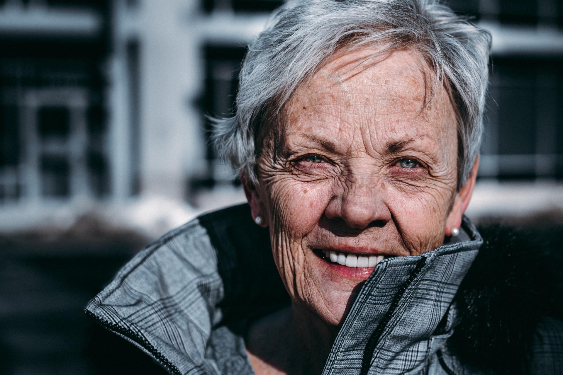 Smiling woman in a gray jacket outdoors, with a blurred building in the background