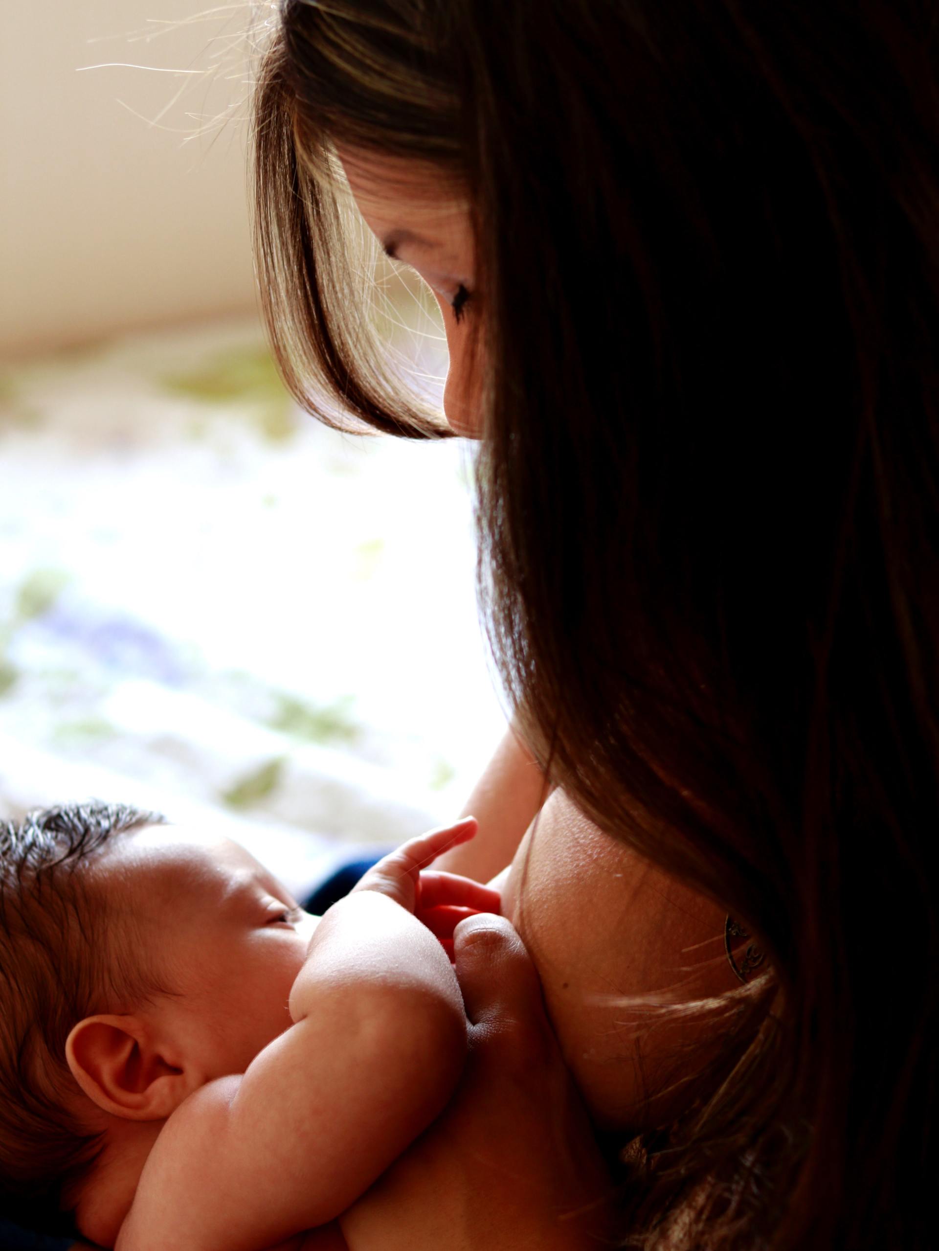 Mother breastfeeding a baby indoors. The mother has dark hair, the baby is nursing peacefully.