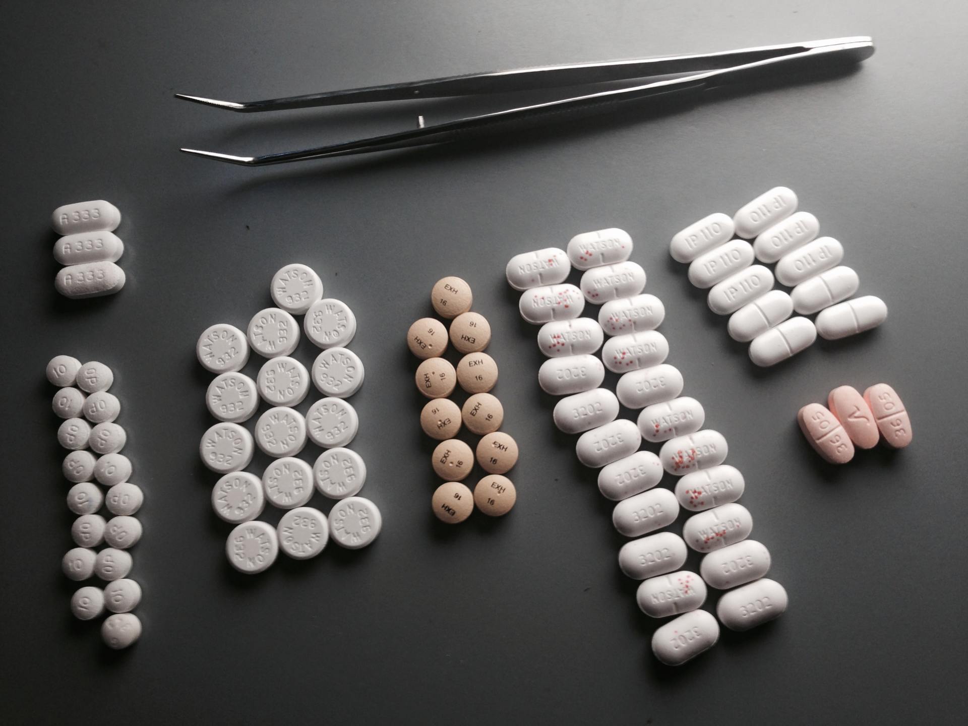 There are many different types of pills and a pair of tweezers on the table.