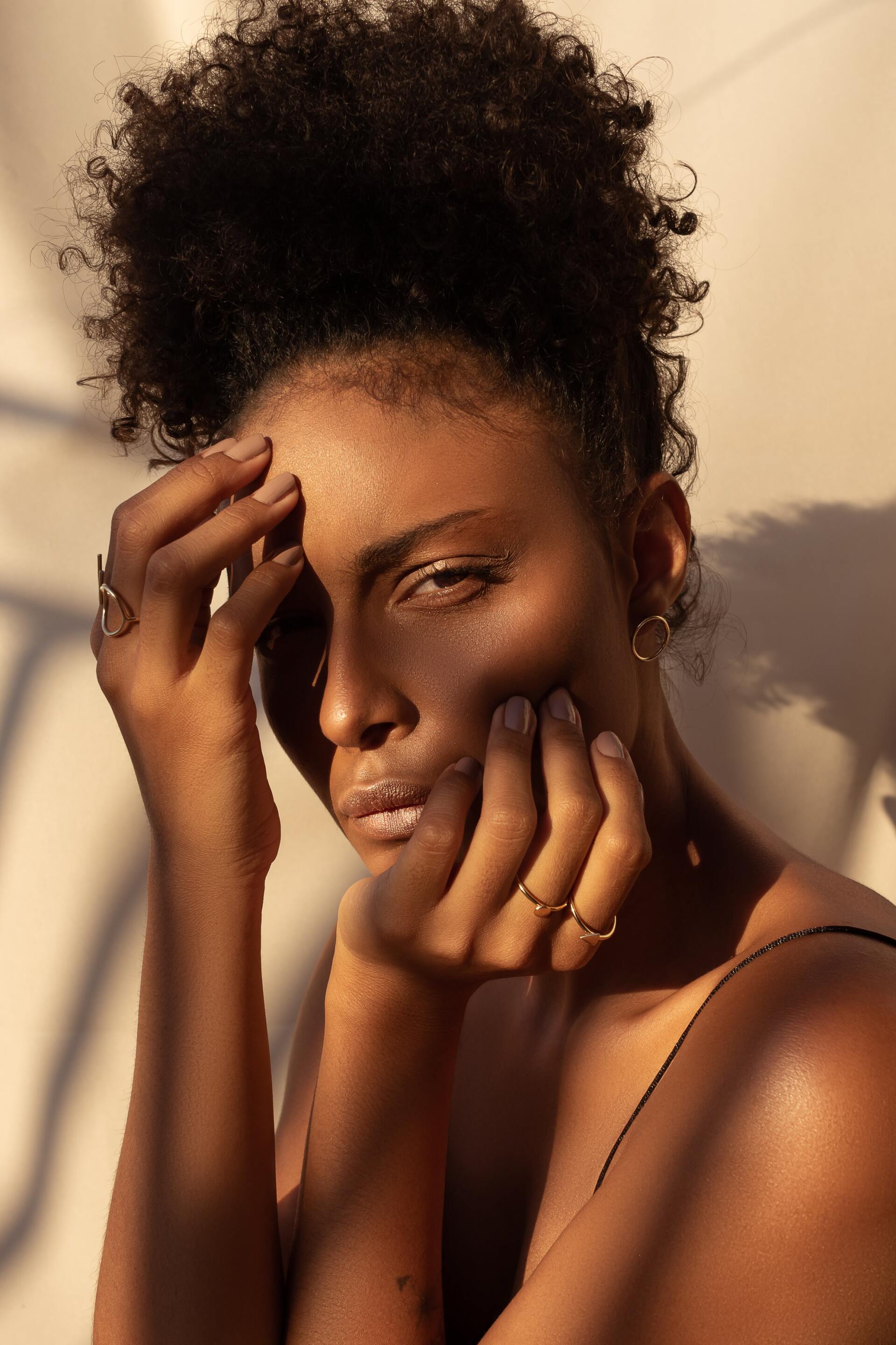 Portrait of a person with curly hair, hand on face, in warm sunlight