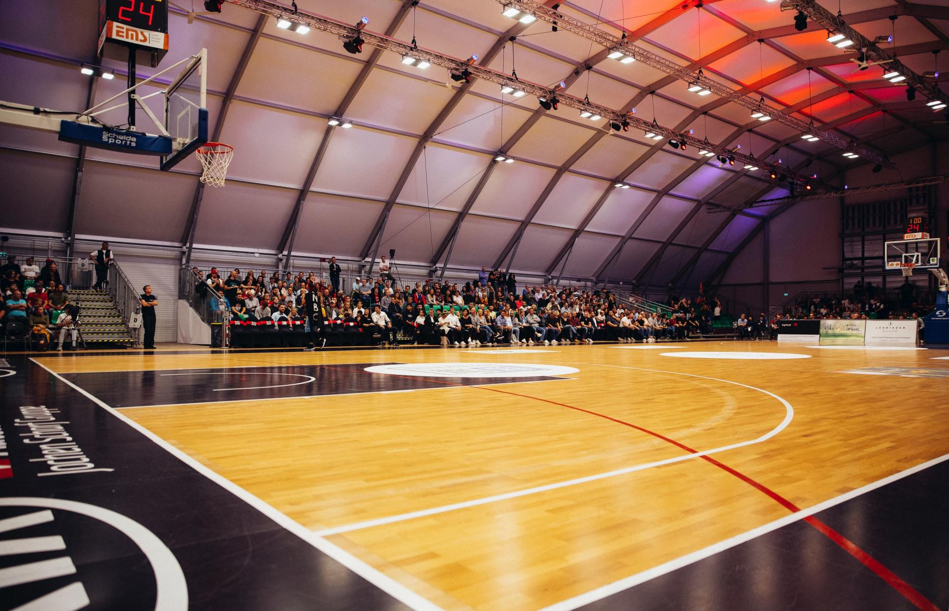 A basketball court in a stadium with a crowd watching a game.