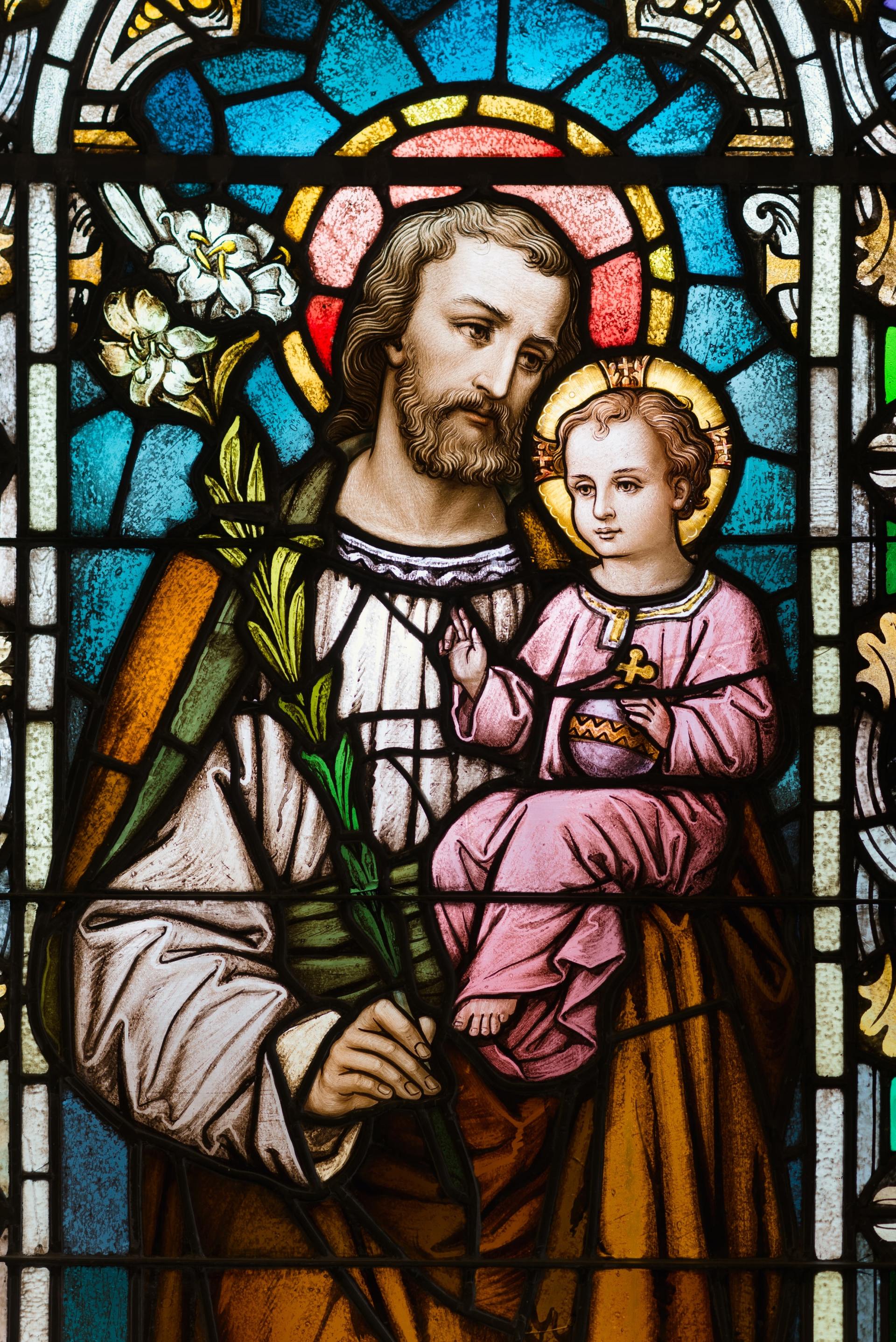 A stained glass window of a man holding a baby jesus.