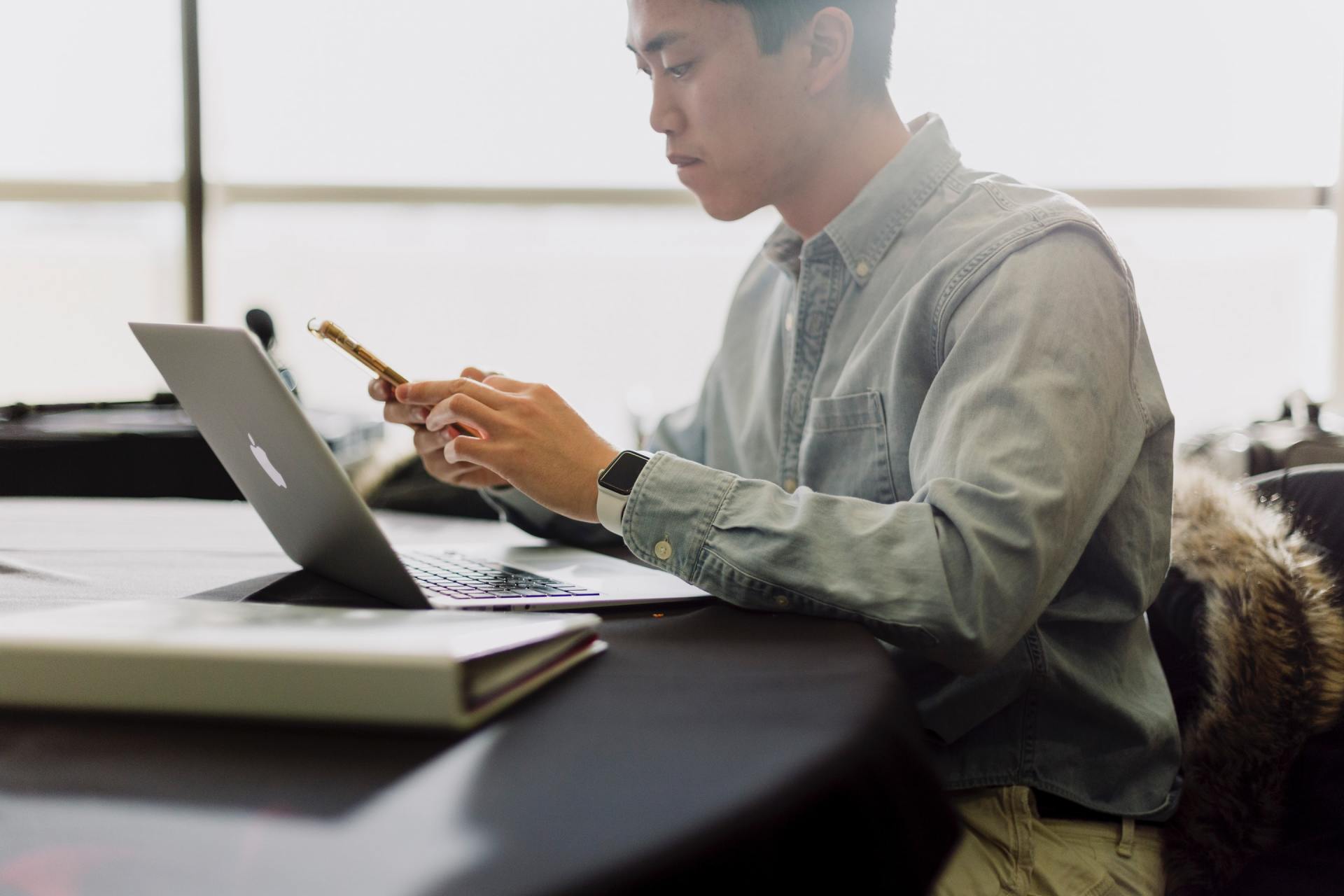 A man is sitting at a table using a laptop and a cell phone.