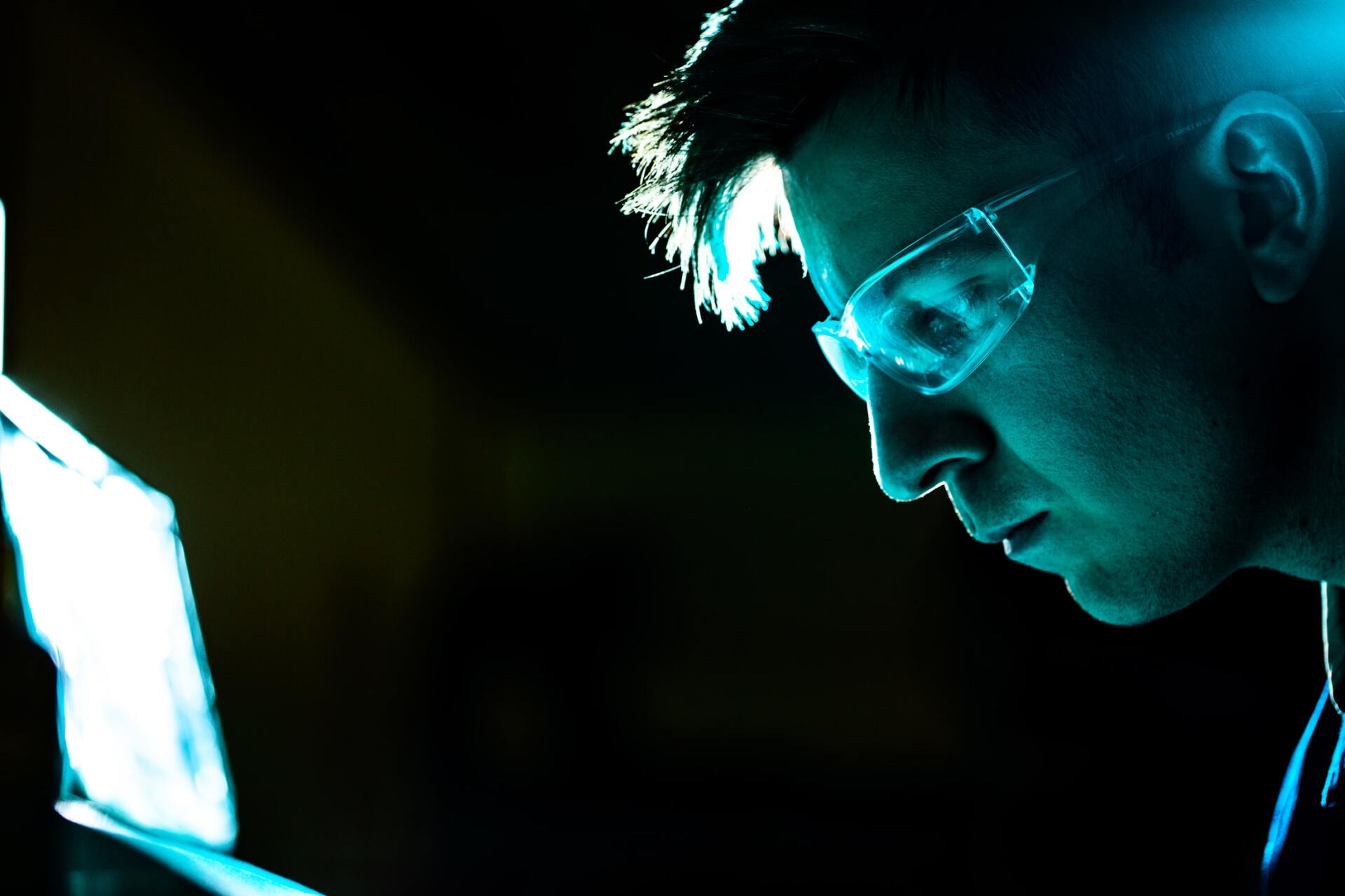 A man wearing glasses is looking at a laptop in the dark.