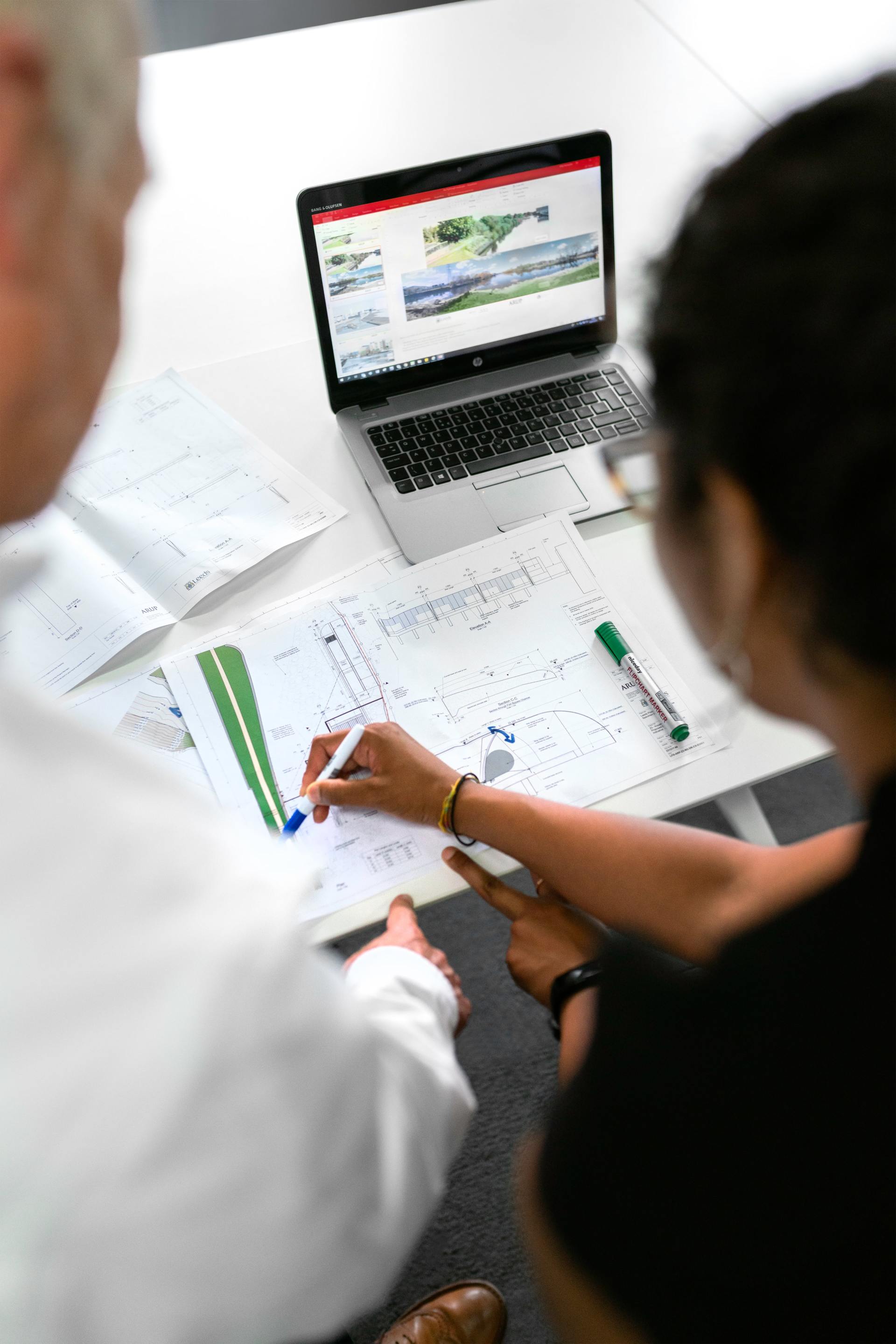 A man and a woman are sitting at a table looking at a laptop showing system architecture
