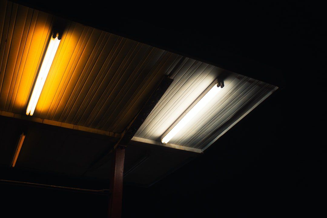 Des lumières fluorescentes jaunes et blanches illuminent un auvent en métal ondulé sur un ciel sombre.