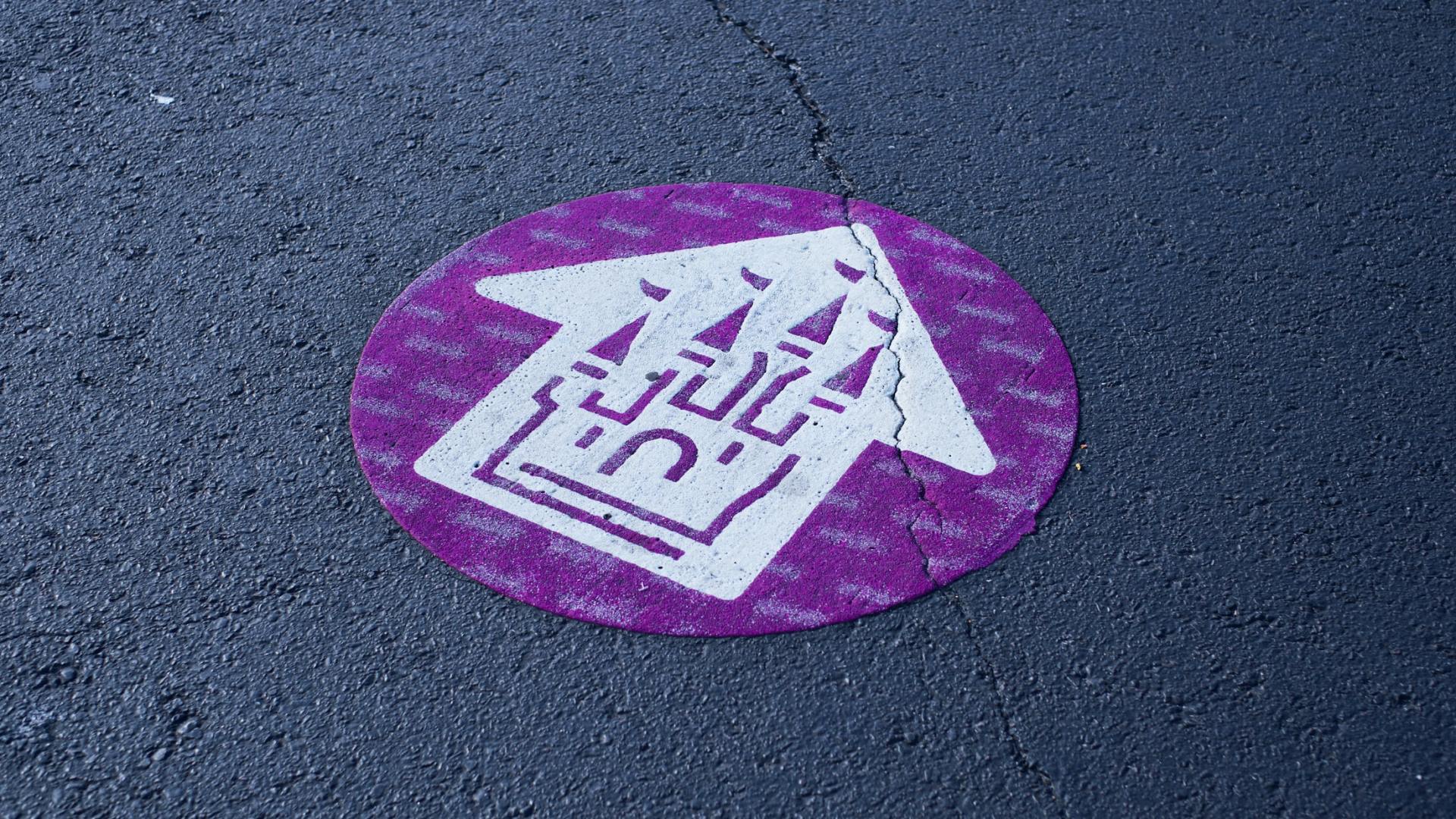 A purple and white circle with an arrow pointing to a castle on the ground.