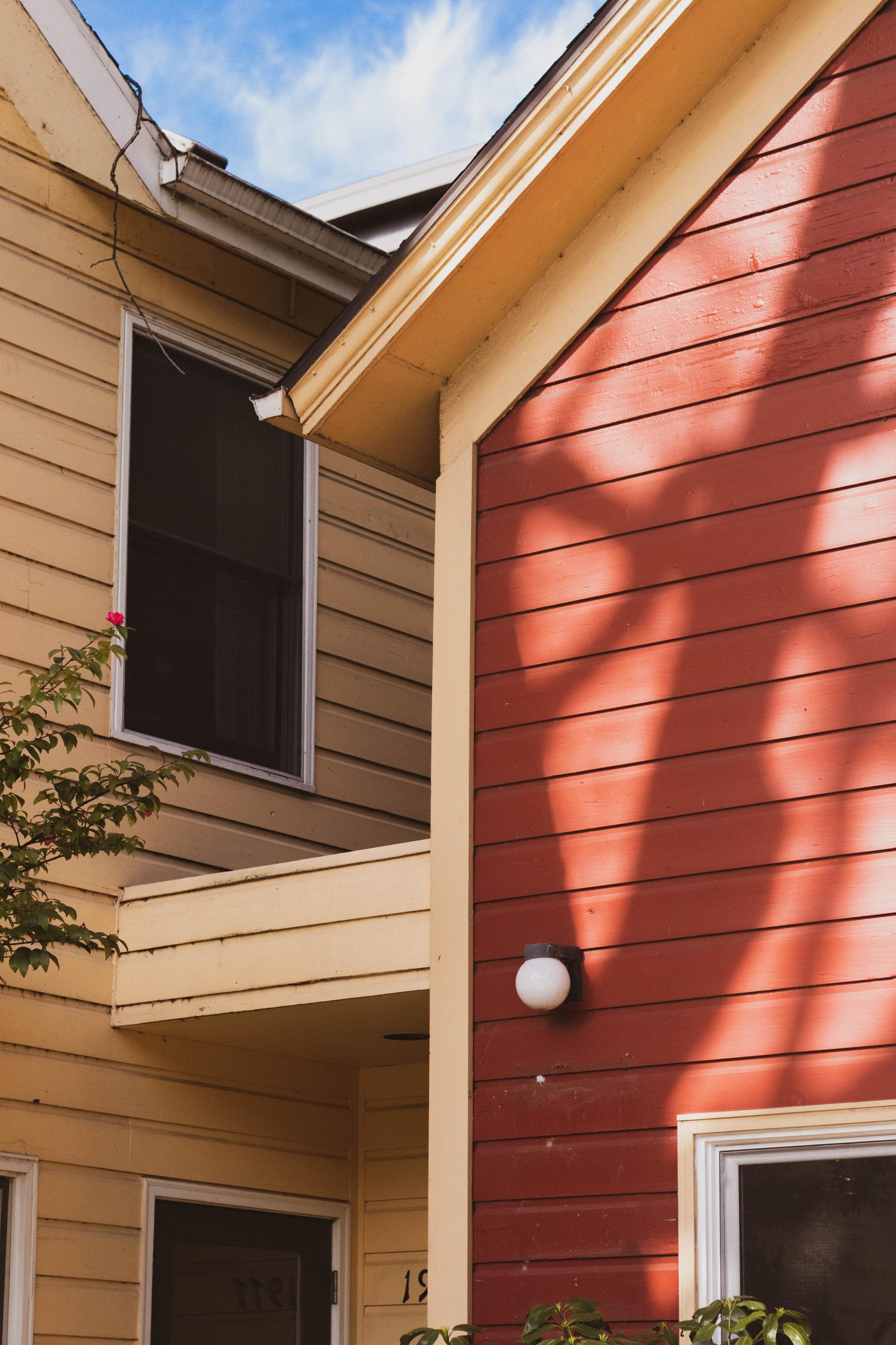 Two-story building exterior. Tan and red siding, white-framed windows, and a round light fixture.