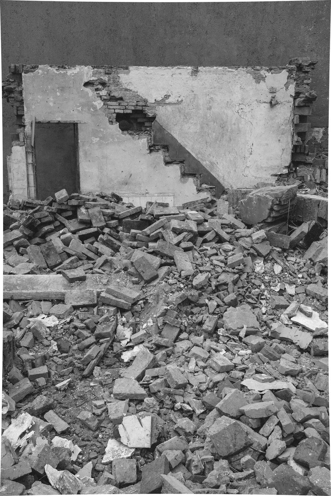 Debris pile in front of a partially demolished building. Stairs visible on the exposed wall.
