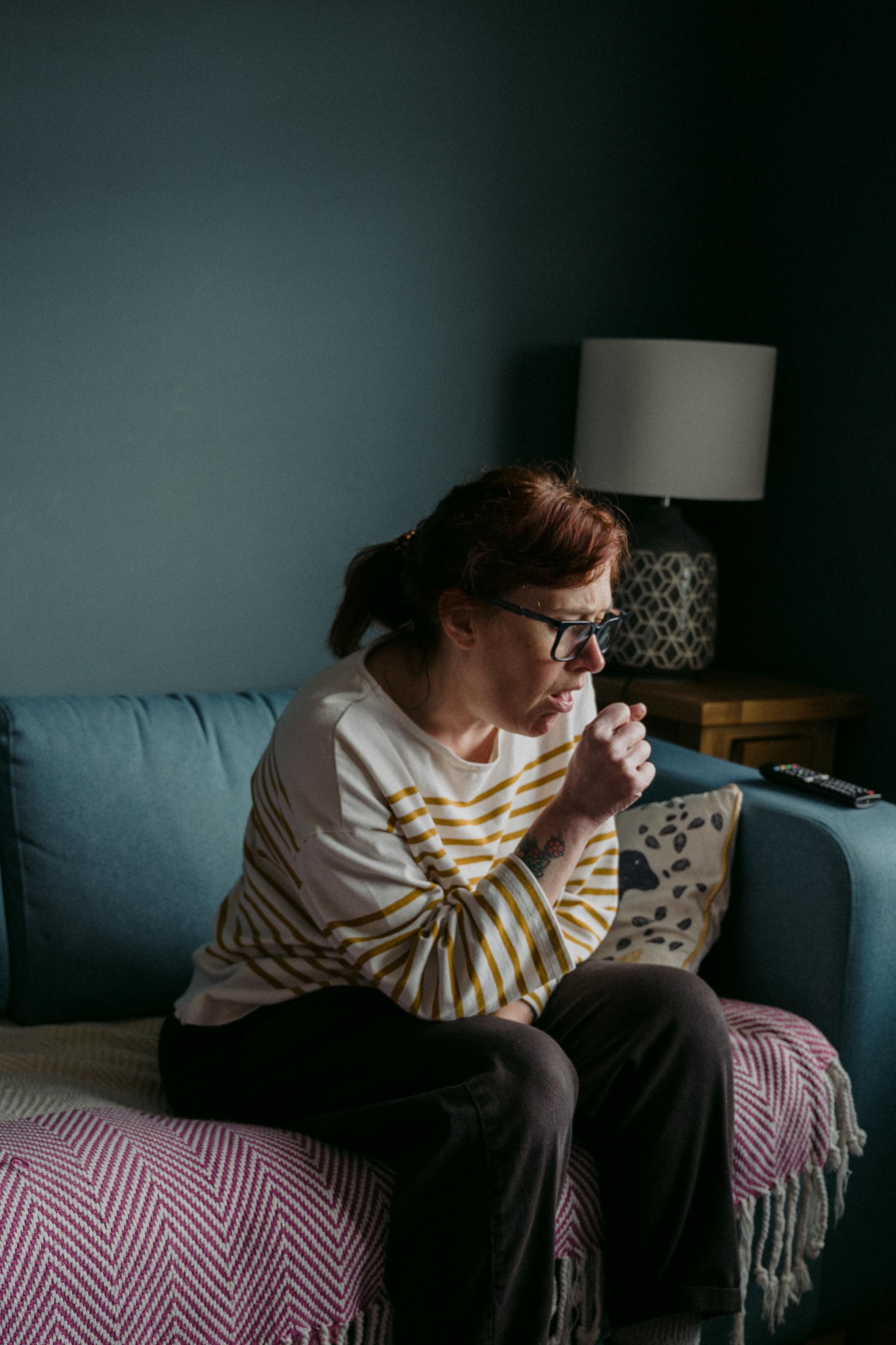 A woman is sitting on a couch coughing.