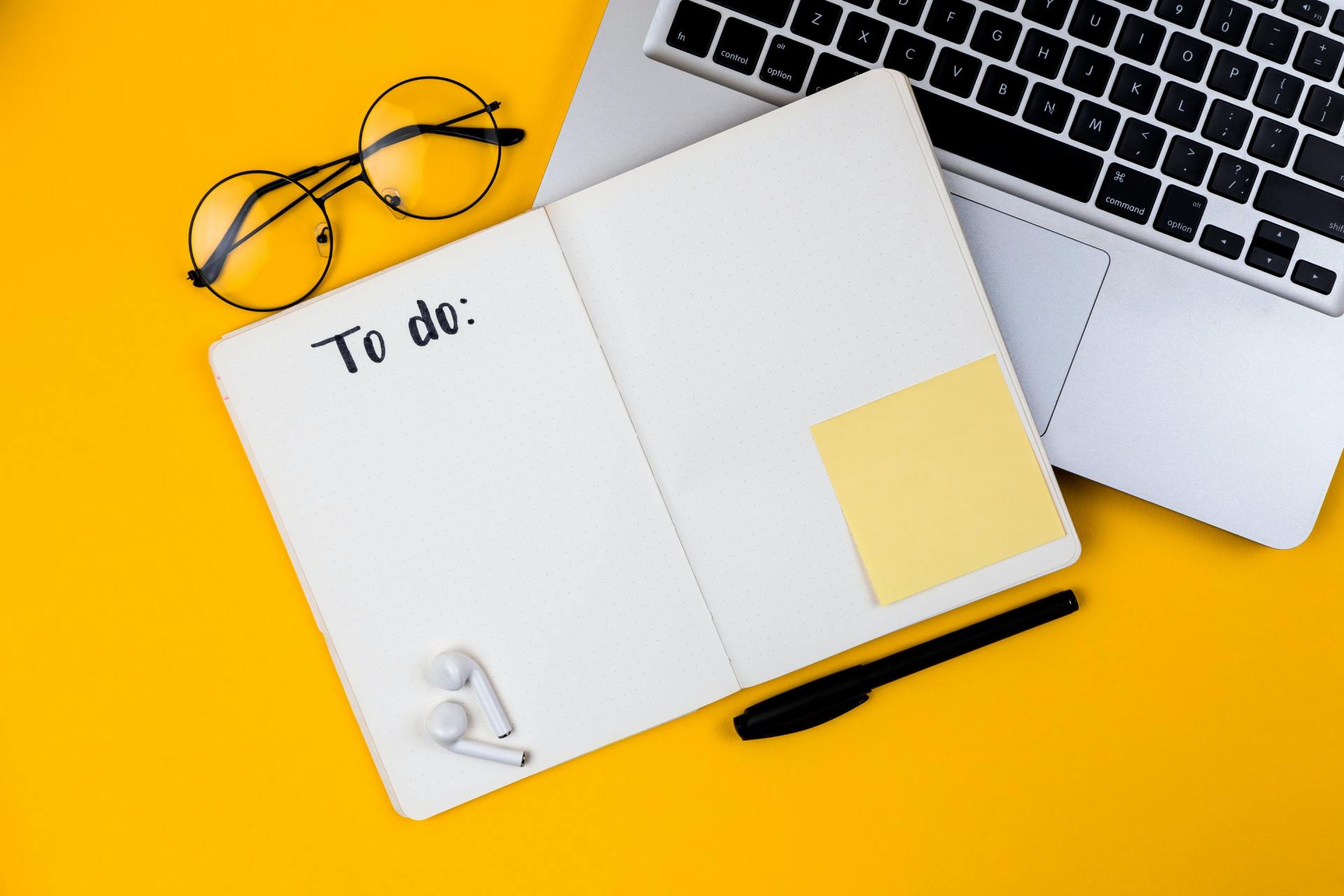 Um caderno com as palavras `` fazer '' escritas nele está sobre uma mesa amarela ao lado de um laptop.